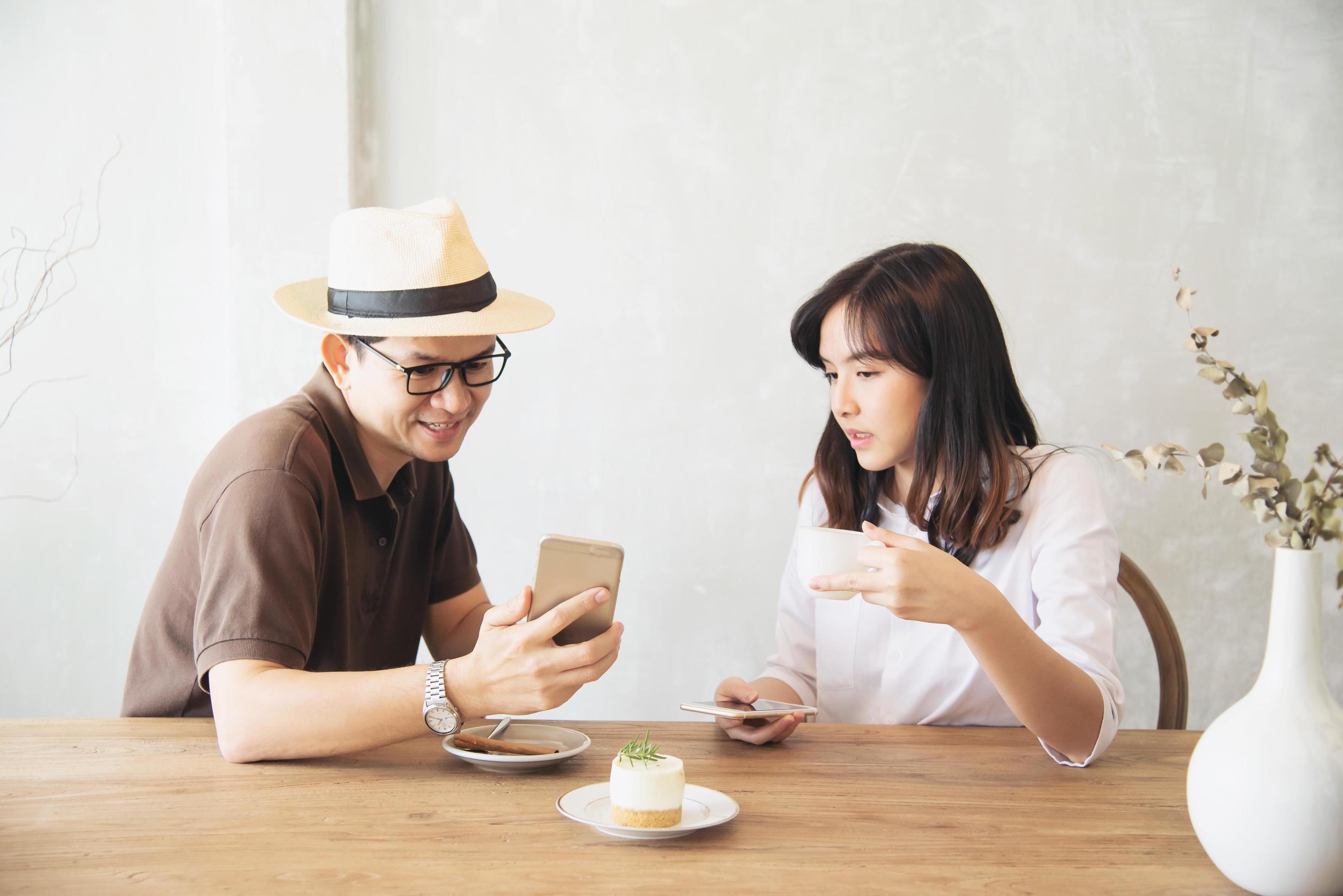 Casual man and woman talking happily while drink coffee and looking mobile phone – happy time lifestyle in coffee shop Stock Free