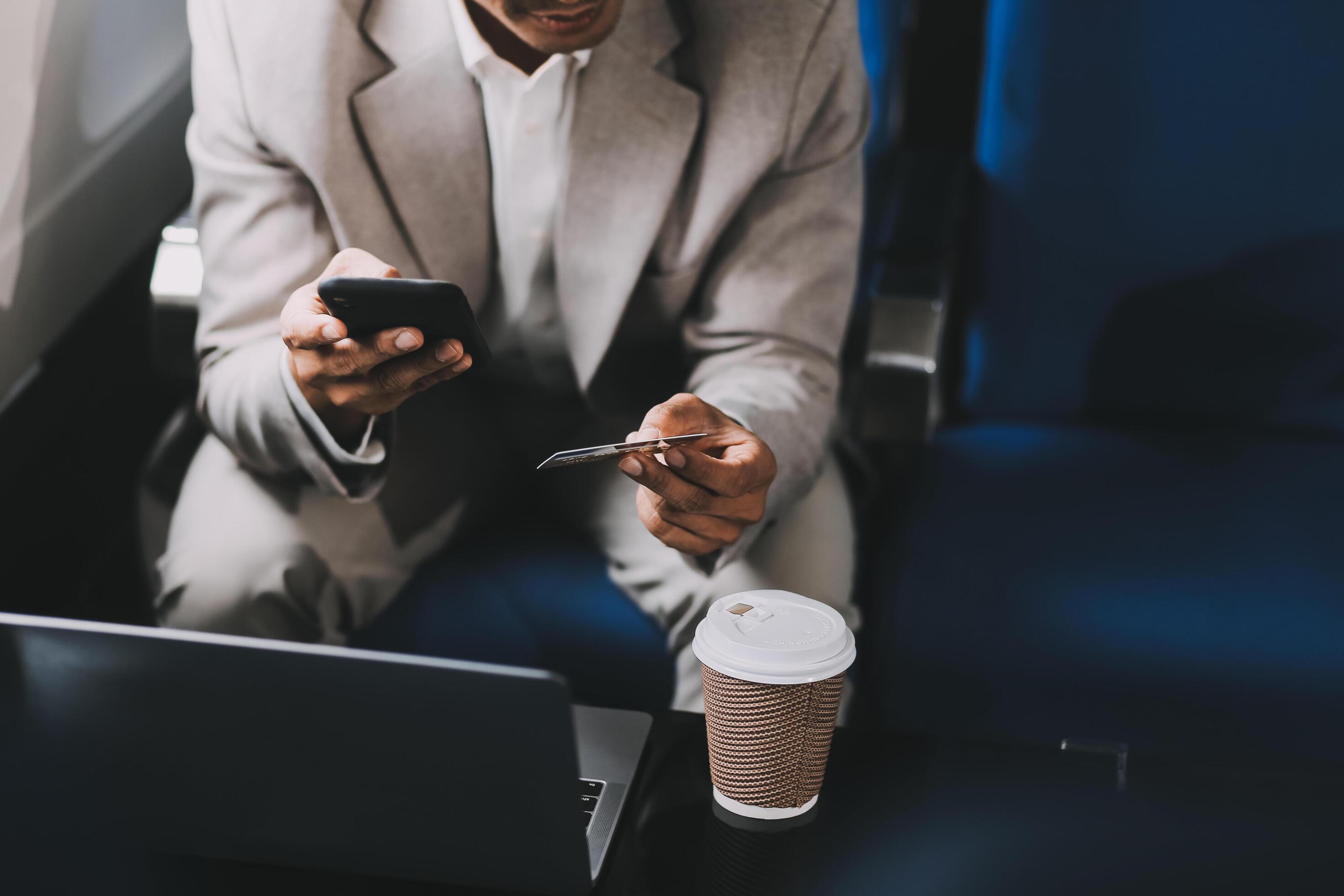 Businessman holding credit card and looking at camera near laptop in private jet Stock Free