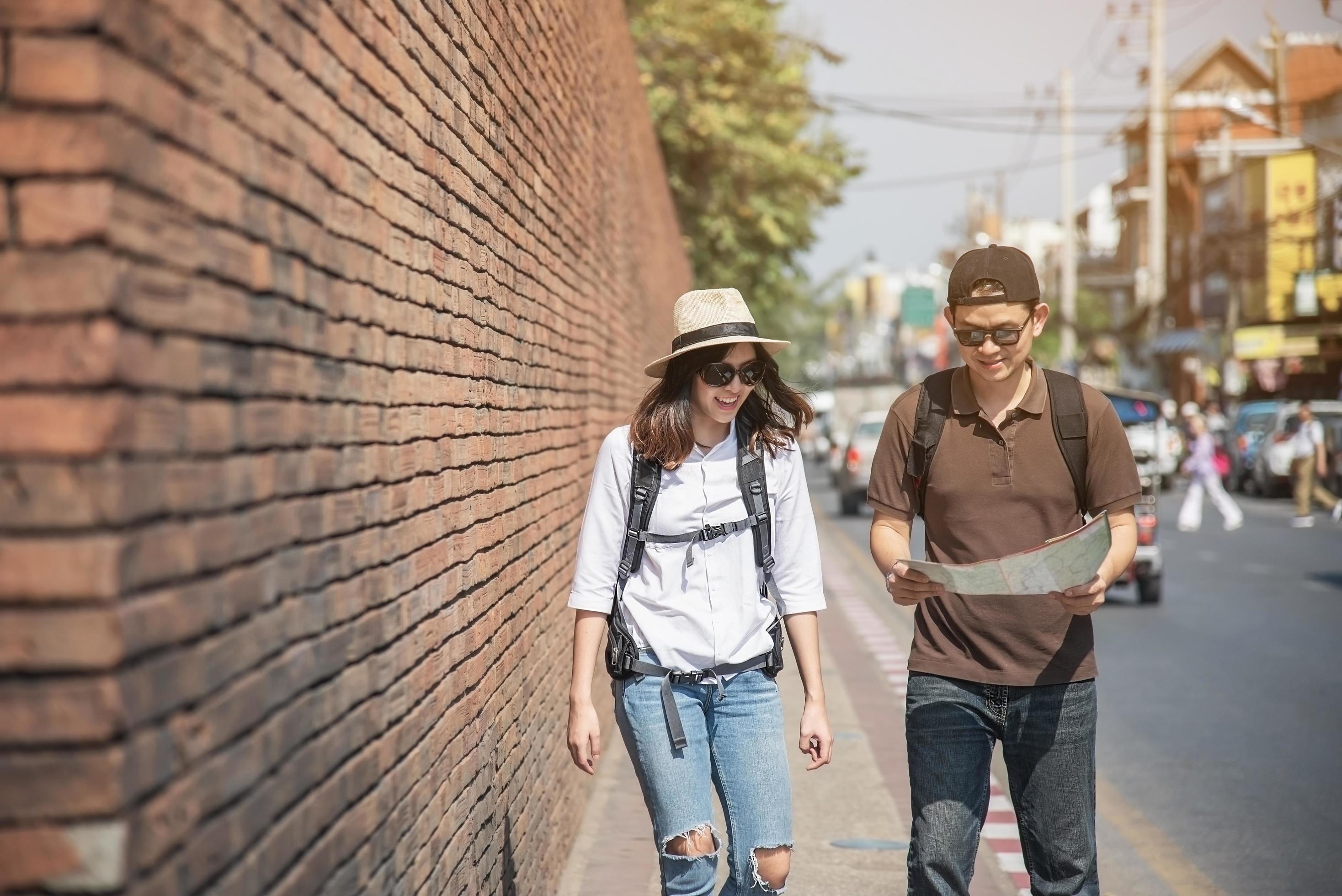 Asian backpack couple tourist holding city map crossing the road – travel people vacation lifestyle concept Stock Free