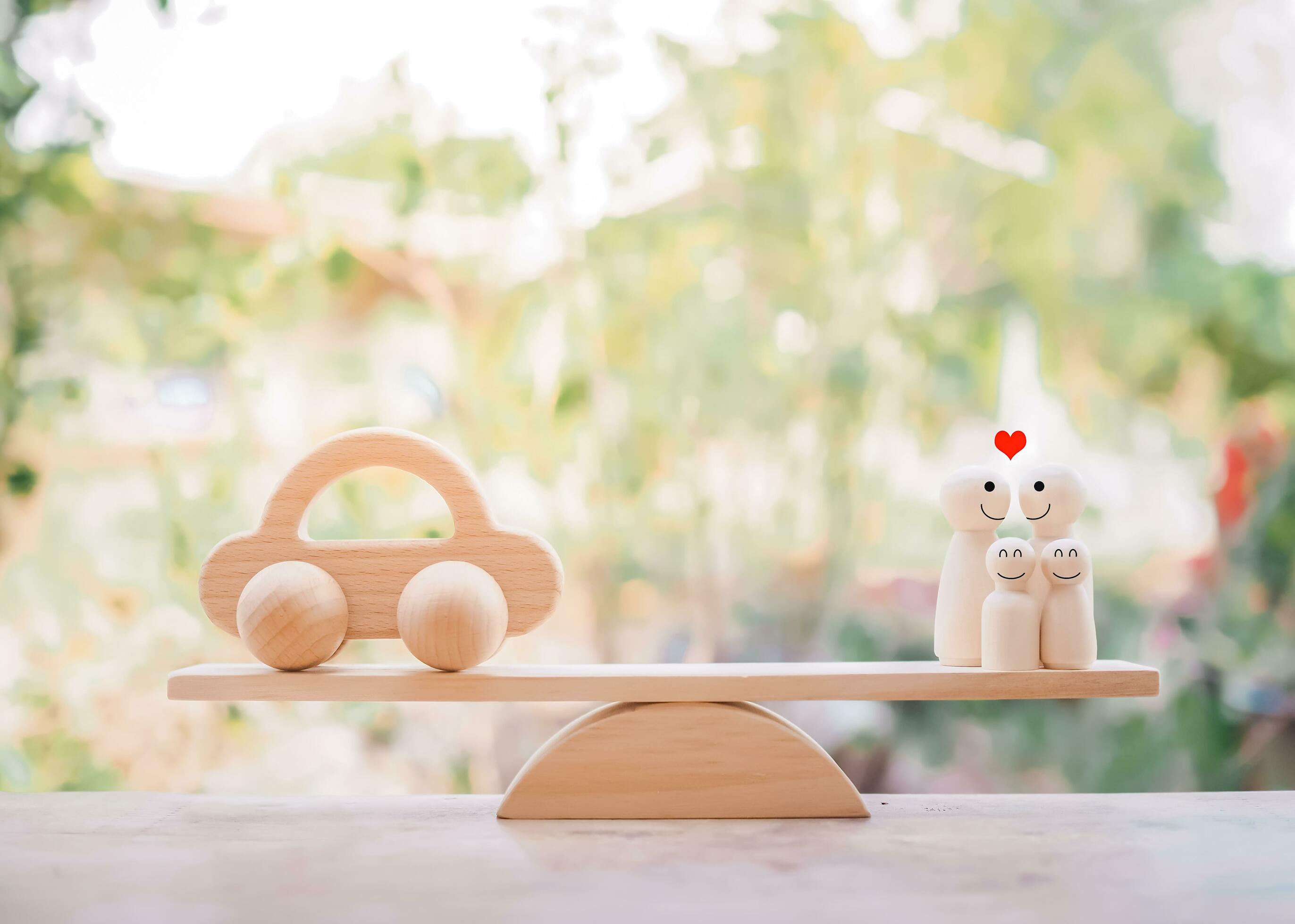 Wooden toy car and wooden figure of family on balancing scale. The concept of saving money buy a car in the future for family. Stock Free