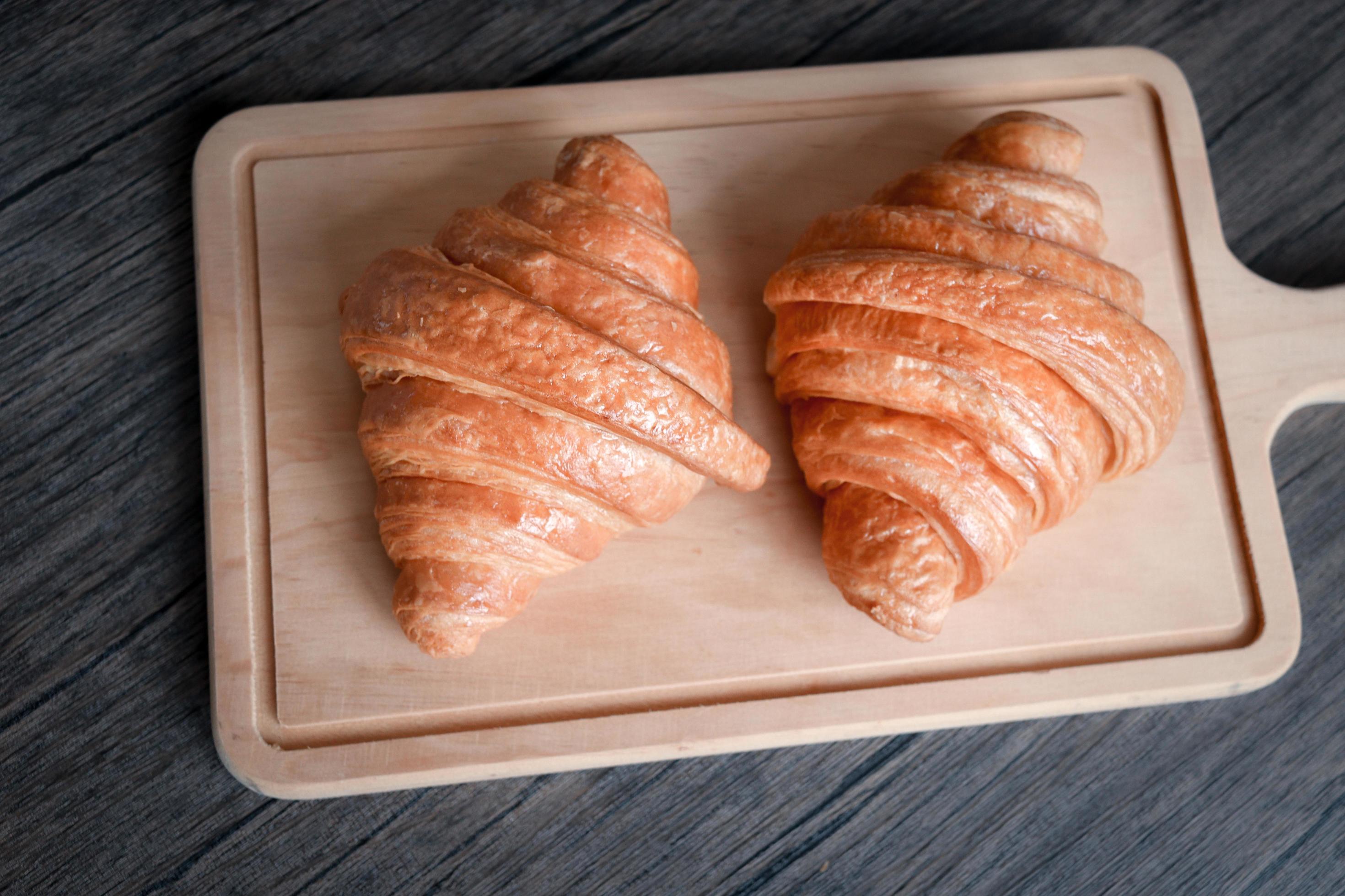 Two freshly baked delicious croissants on wooden cutting board, food on breakfast table Stock Free