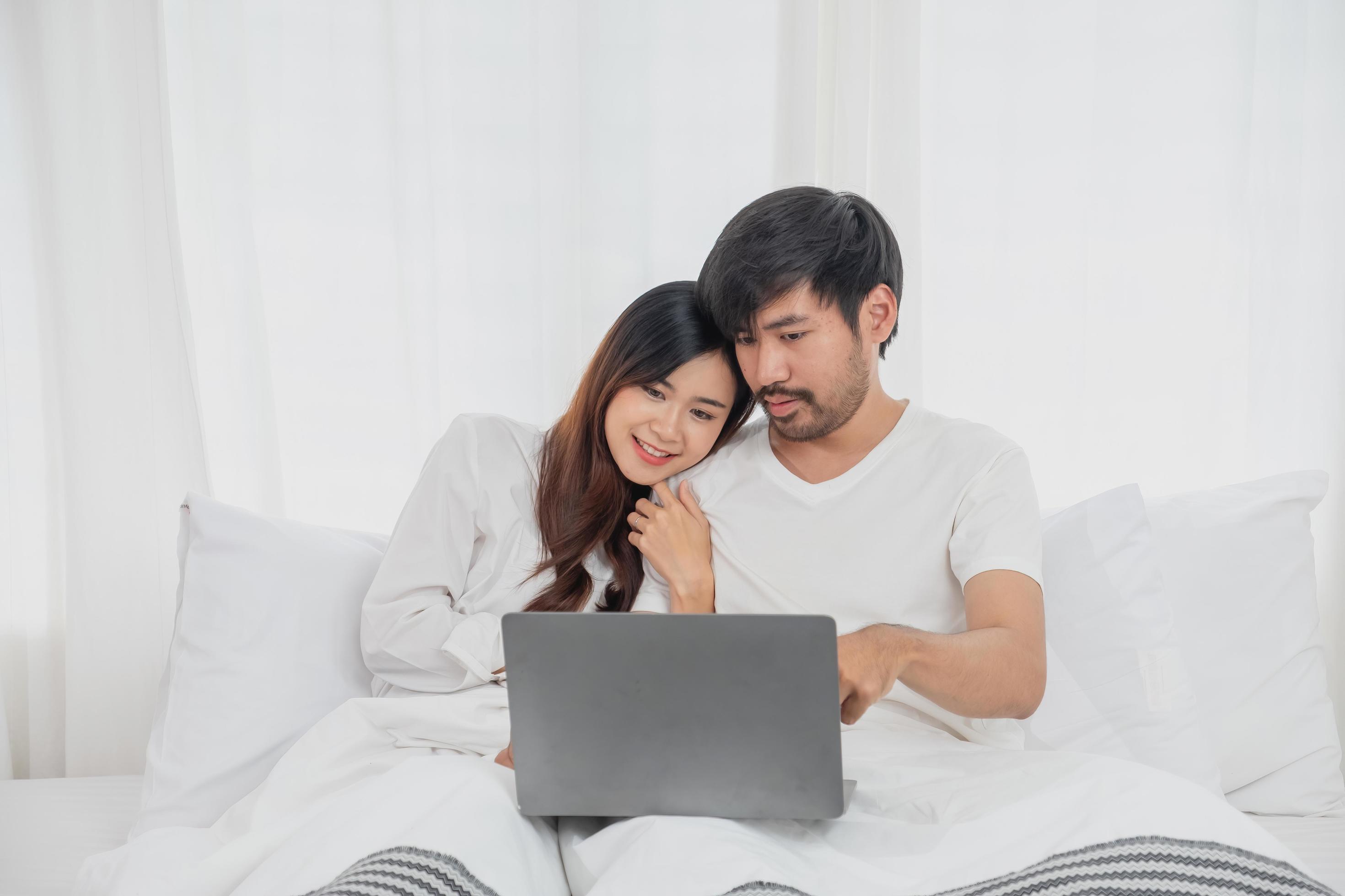 Young happy asian couple using laptop in bed watching movie, romantic time to enhance family relationship, family concept. Stock Free