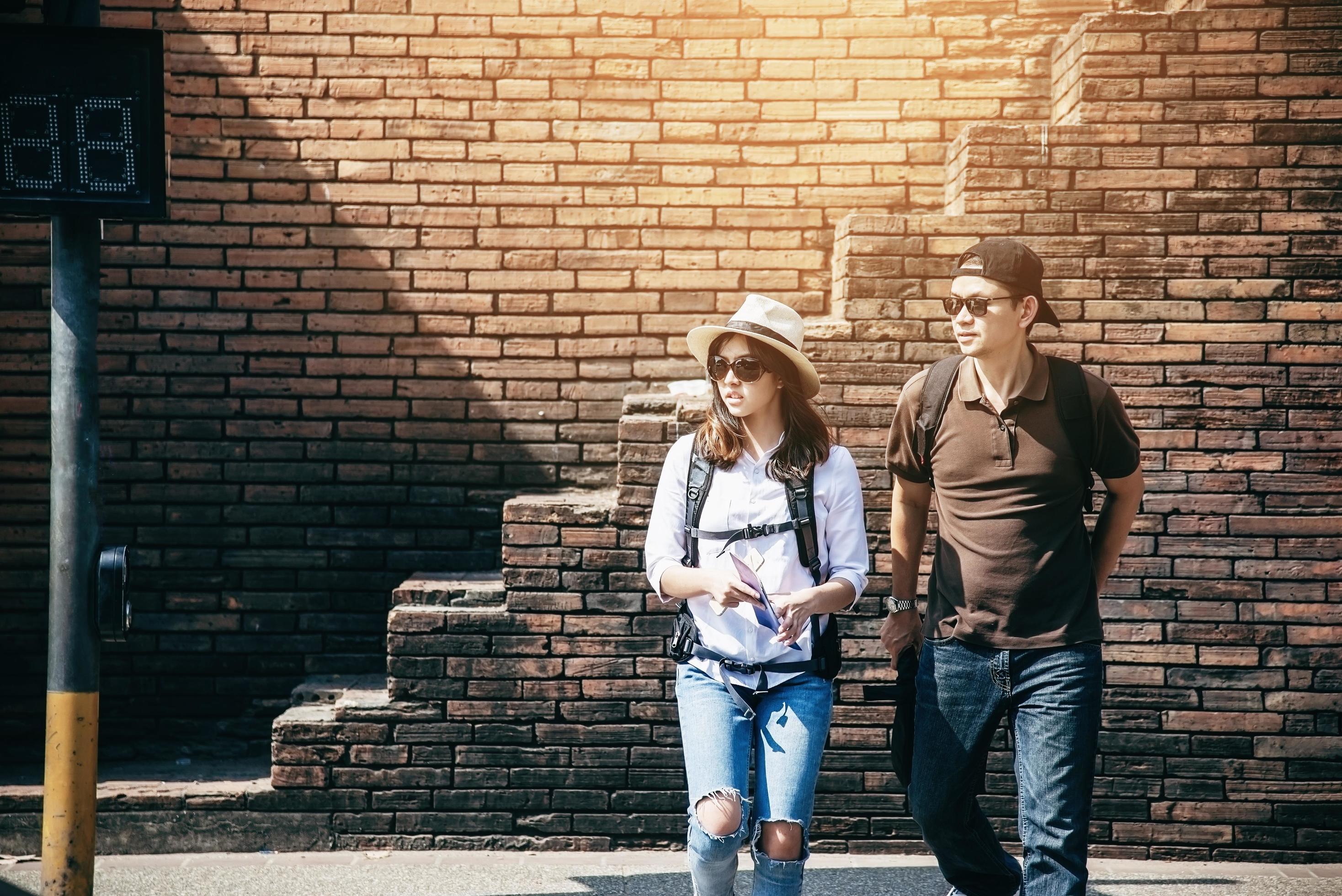 Asian backpack couple tourist holding city map crossing the road – travel people vacation lifestyle concept Stock Free