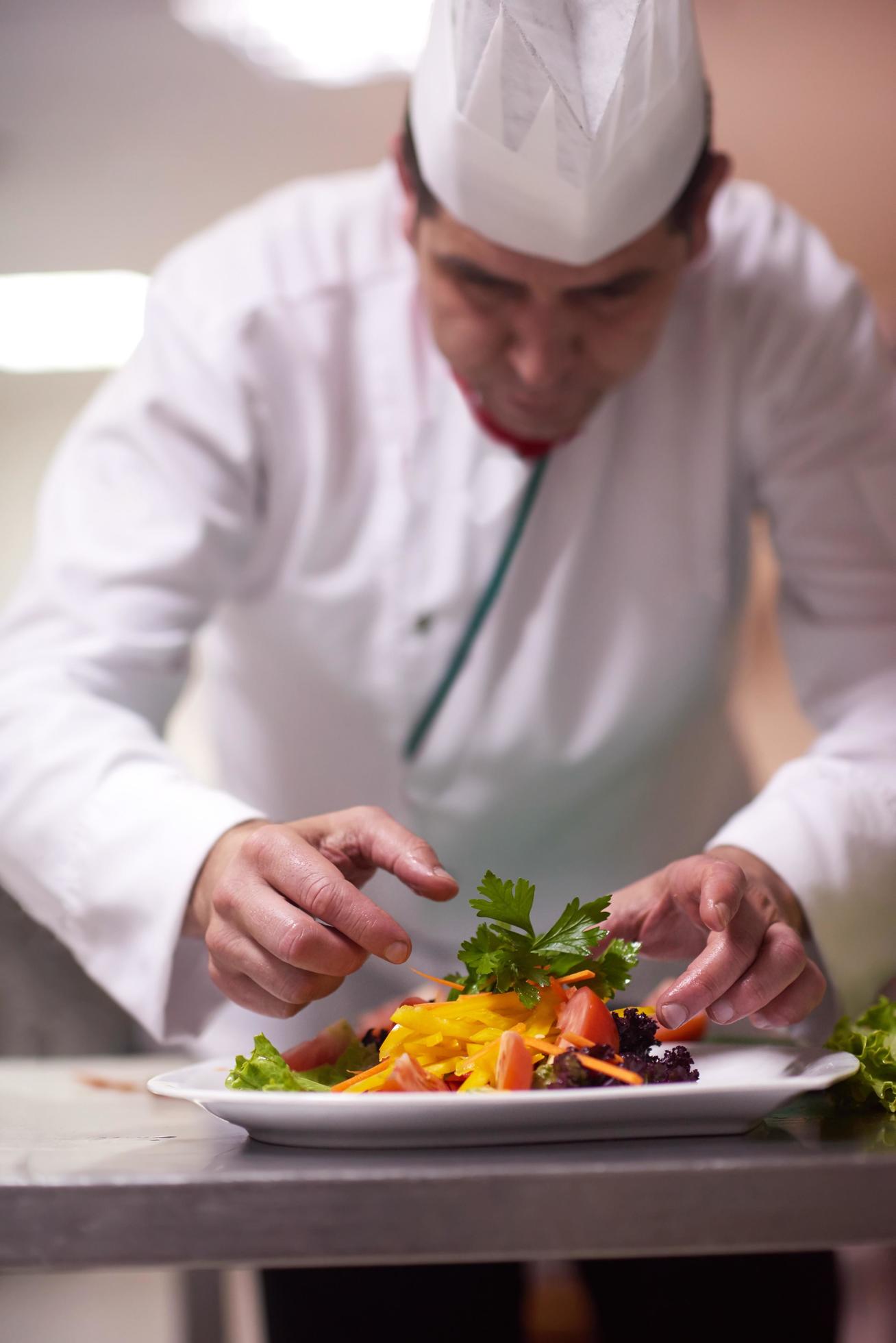 chef in hotel kitchen preparing and decorating food Stock Free