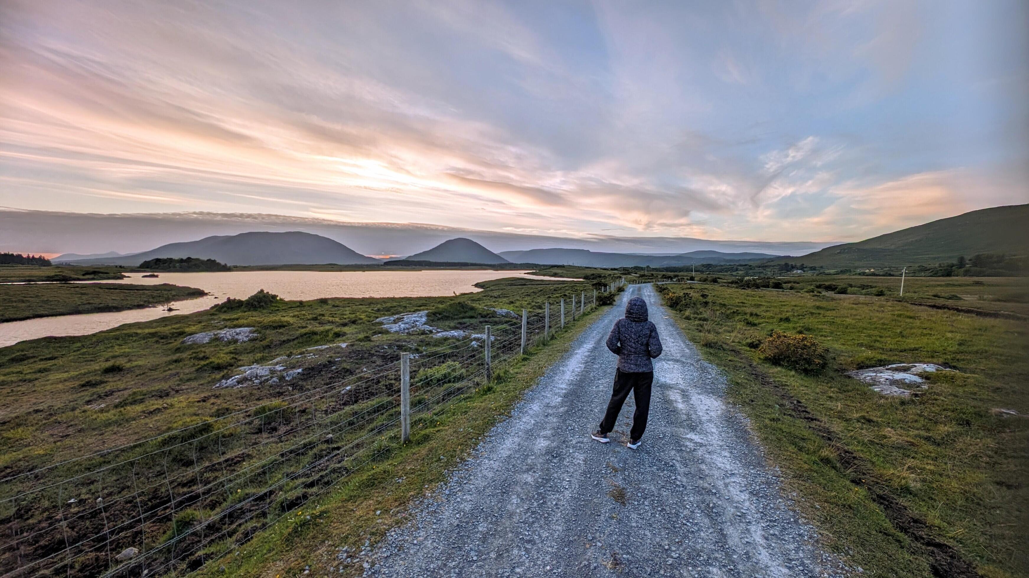 Girl hiker on Empty rural road by lake and mountains at Connemara national park, Galway, Ireland Stock Free