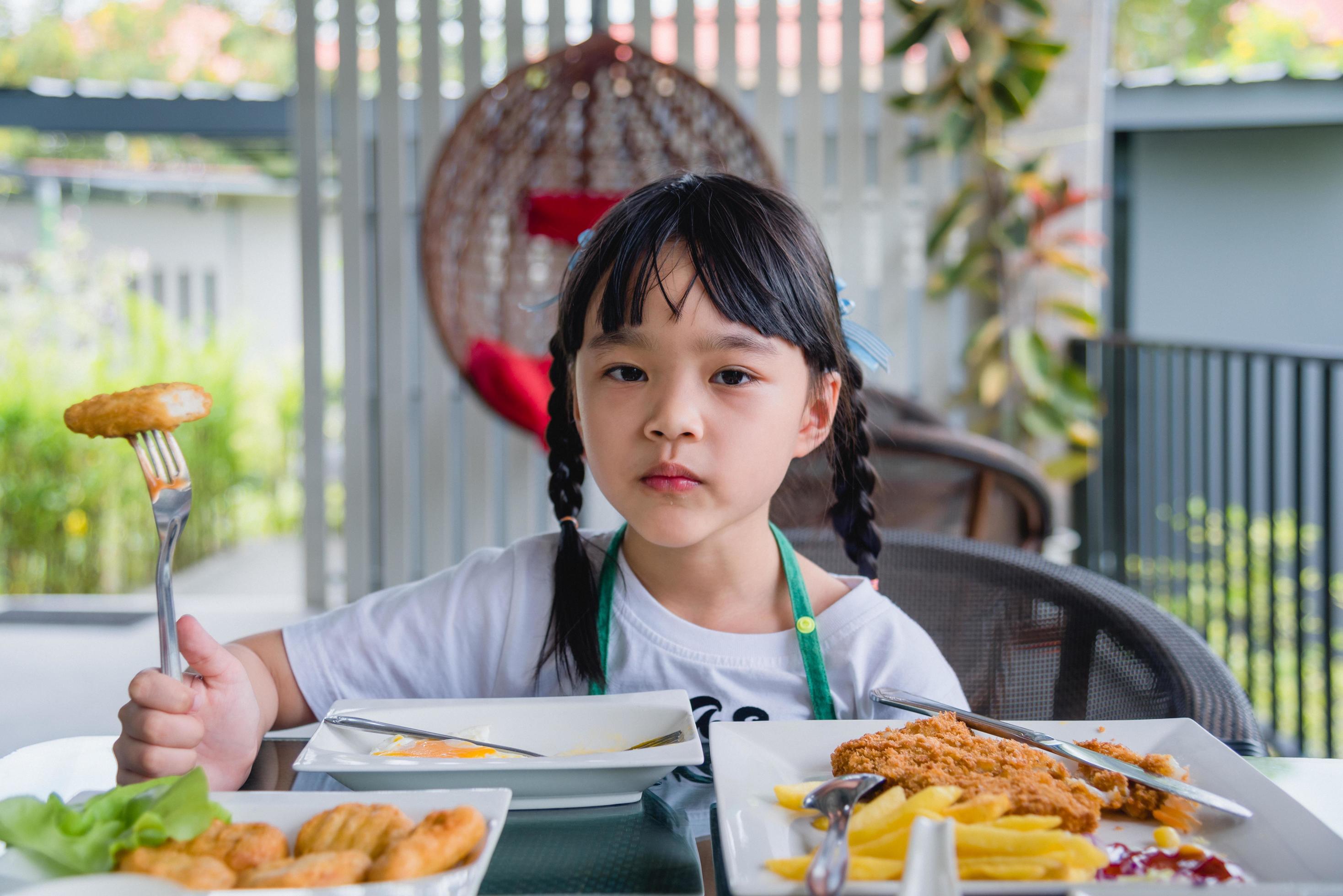 Asian young girl Eating Chicken nuggets fast food on table. Stock Free