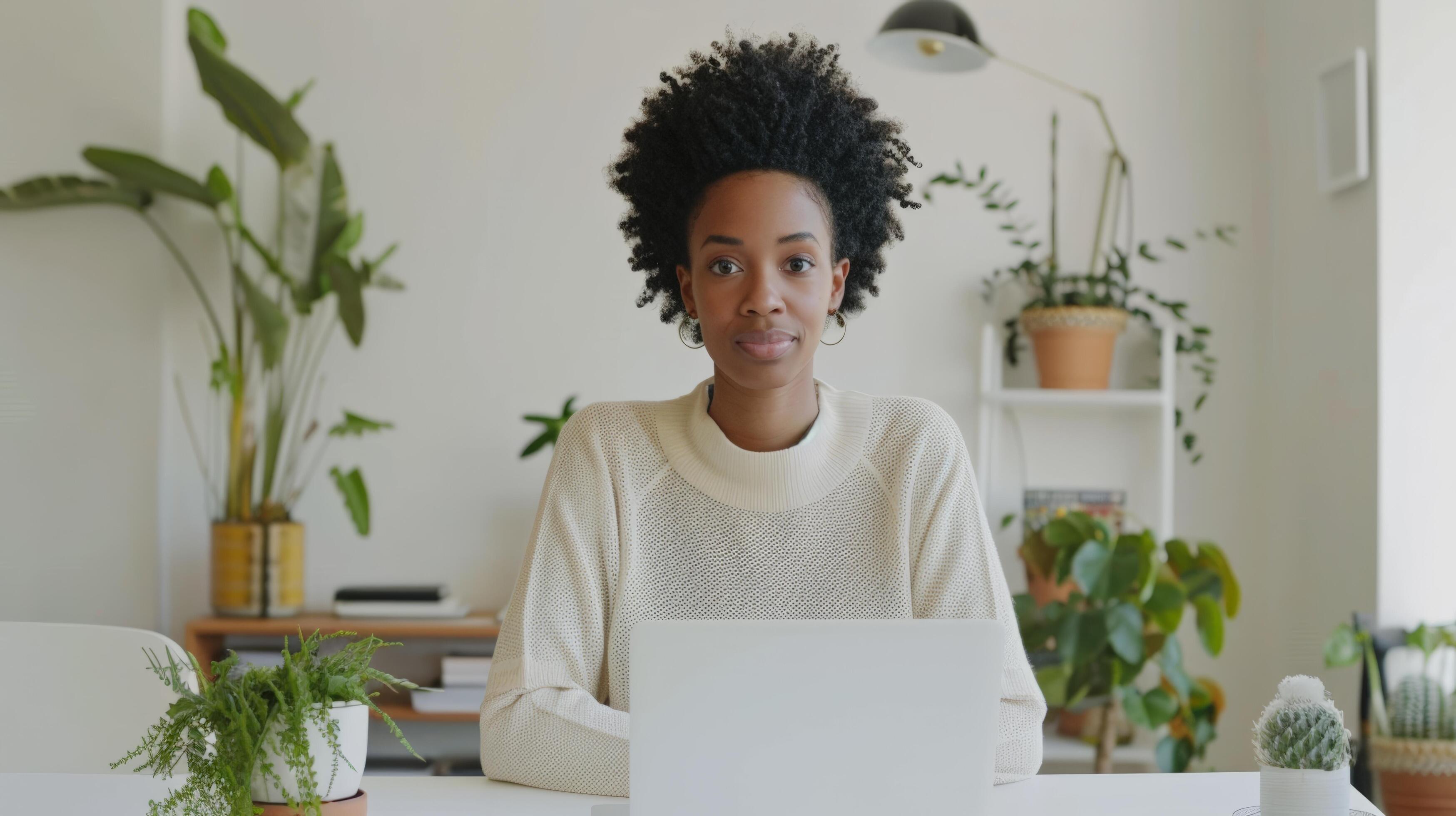 Confident woman working on laptop in cozy home office surrounded by plants, exuding serenity and focus. Stock Free