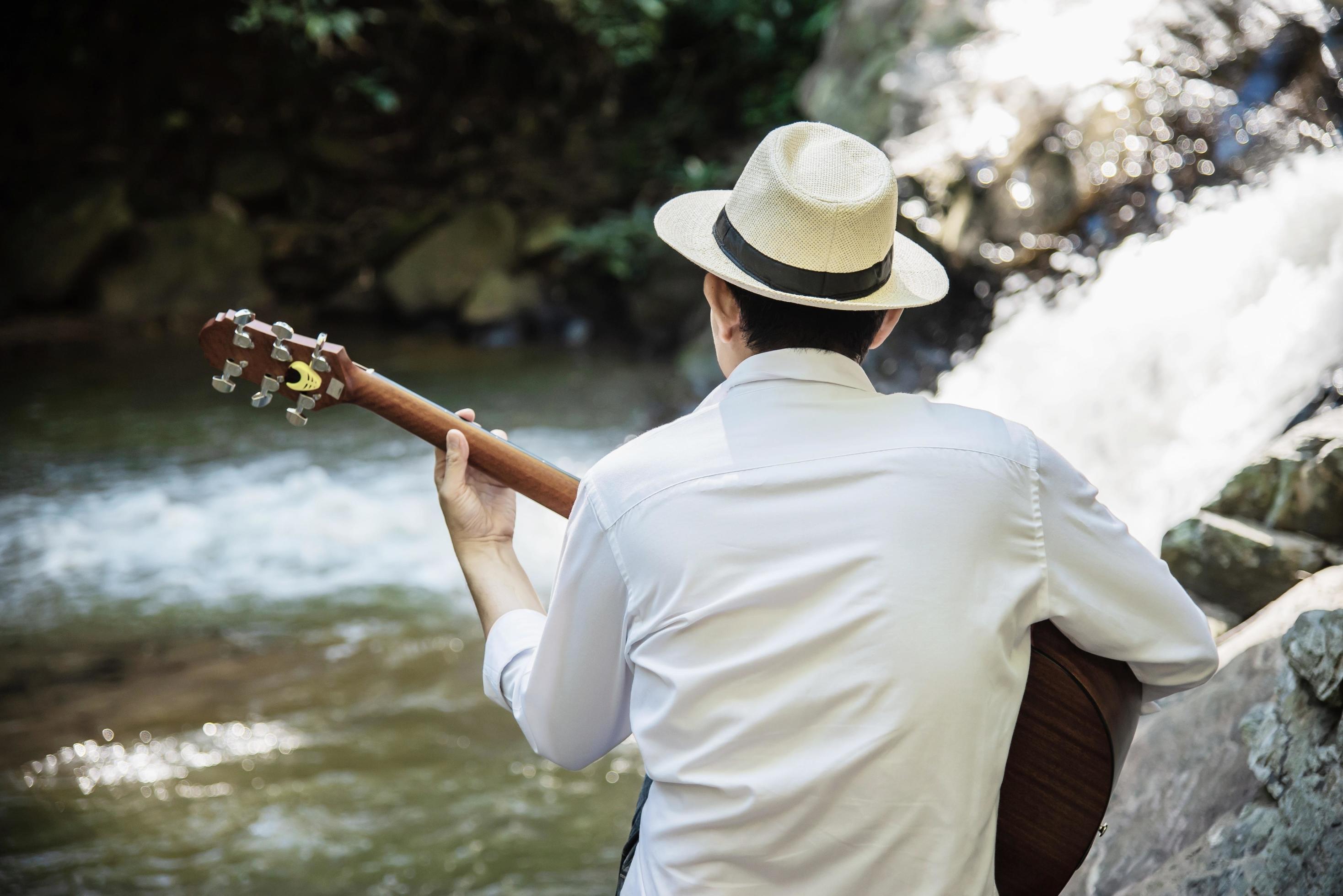 Man play ukulele new to the waterfall – people and music instrument life style in nature concept Stock Free