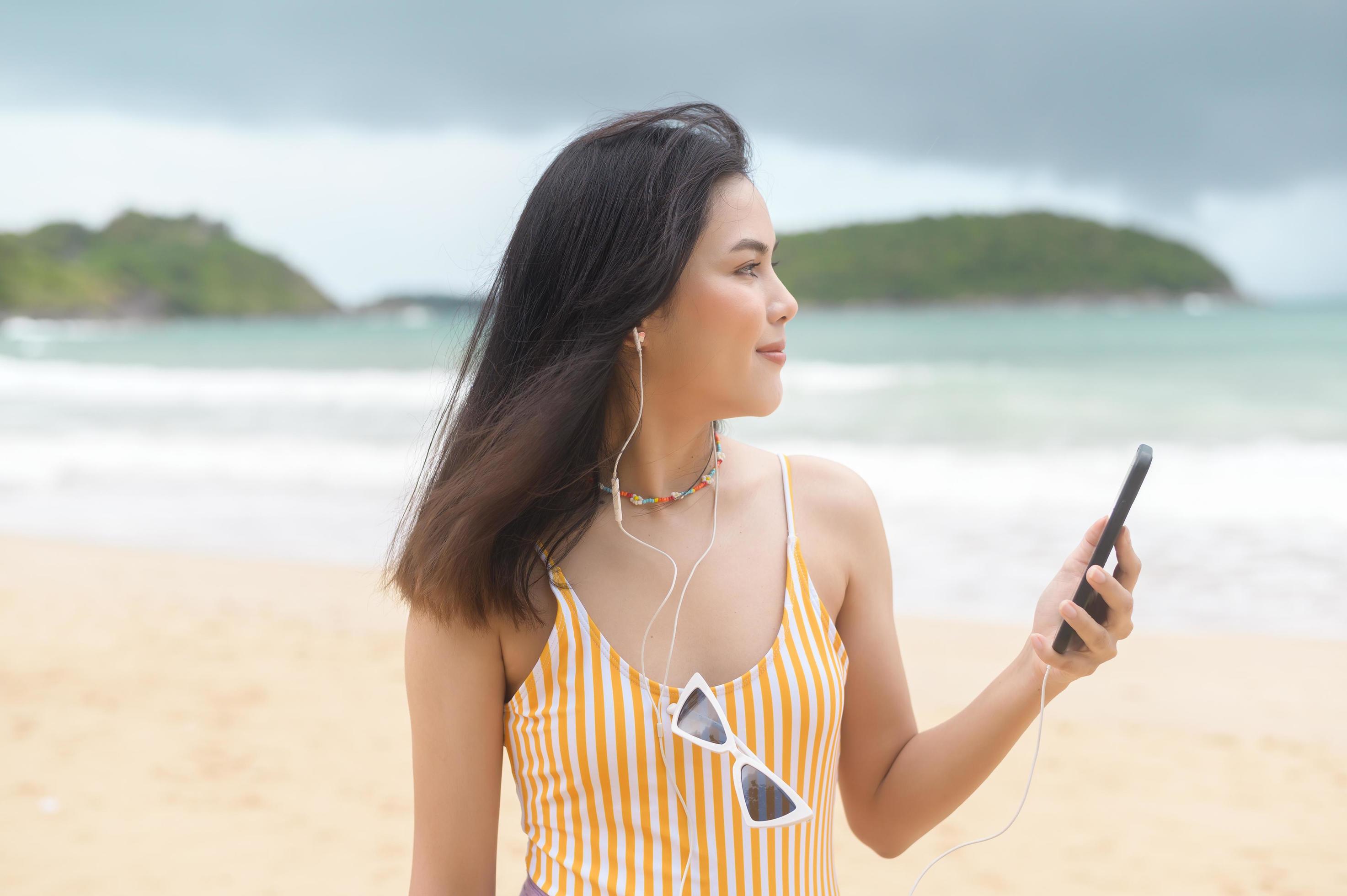 Young Beautiful woman in Bikini listening to music and using smartphone on the beach, Summer, vacation, holidays, Lifestyles concept. Stock Free