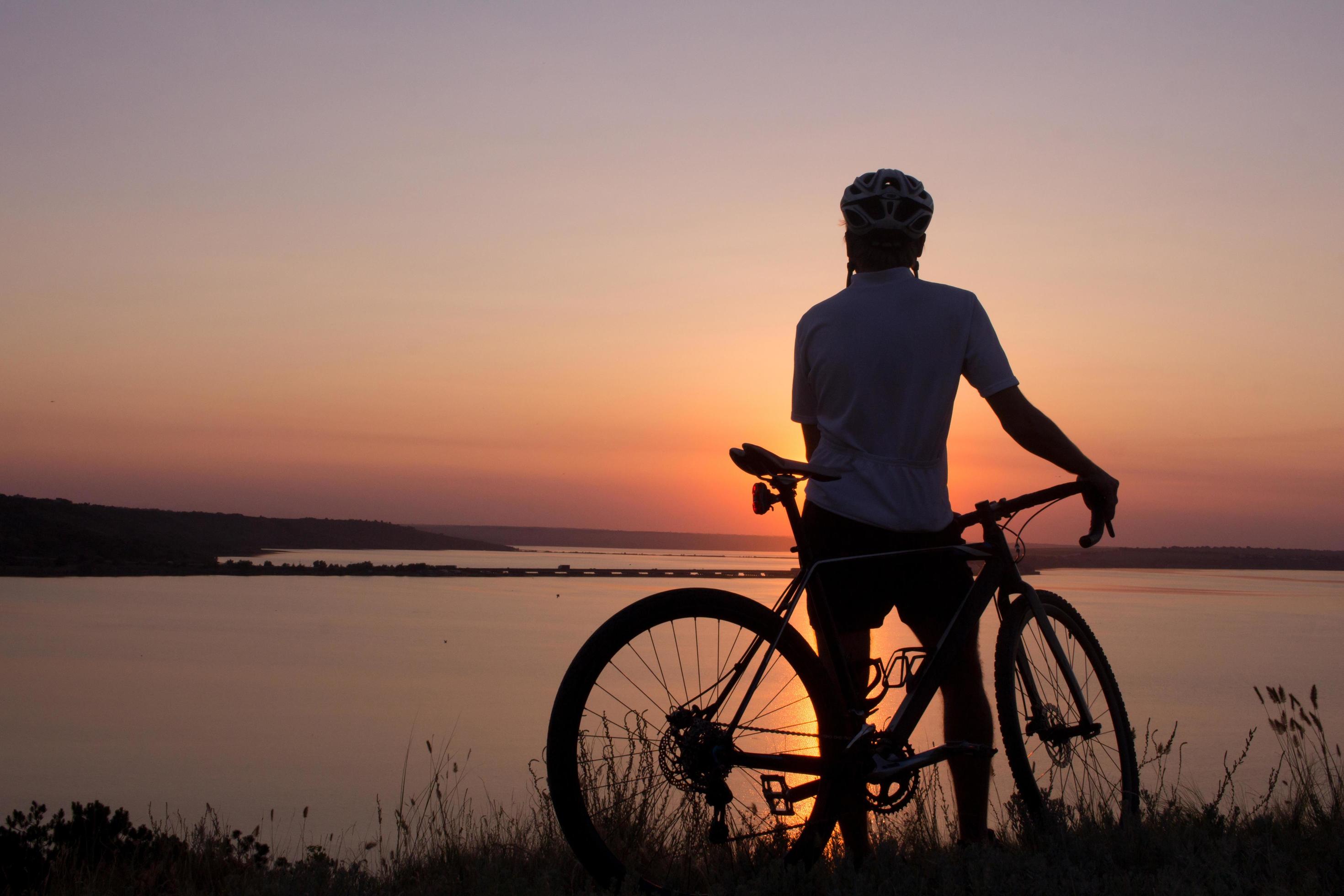 silhouette of a cyclist watching sunset in lake, male bicycle rider in helmet during sunset Stock Free