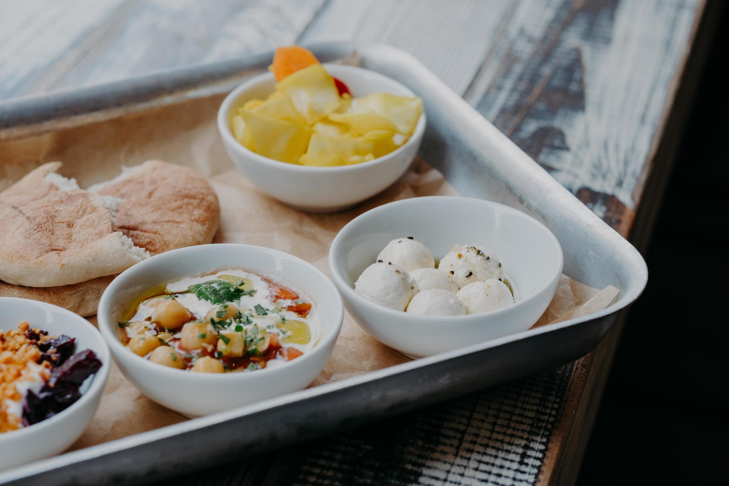 Tasty traditional dish concept. Cropped shot of tray with goat cheese, pita bread, grilled beetroot in bowls on wooden table. Israel food Stock Free