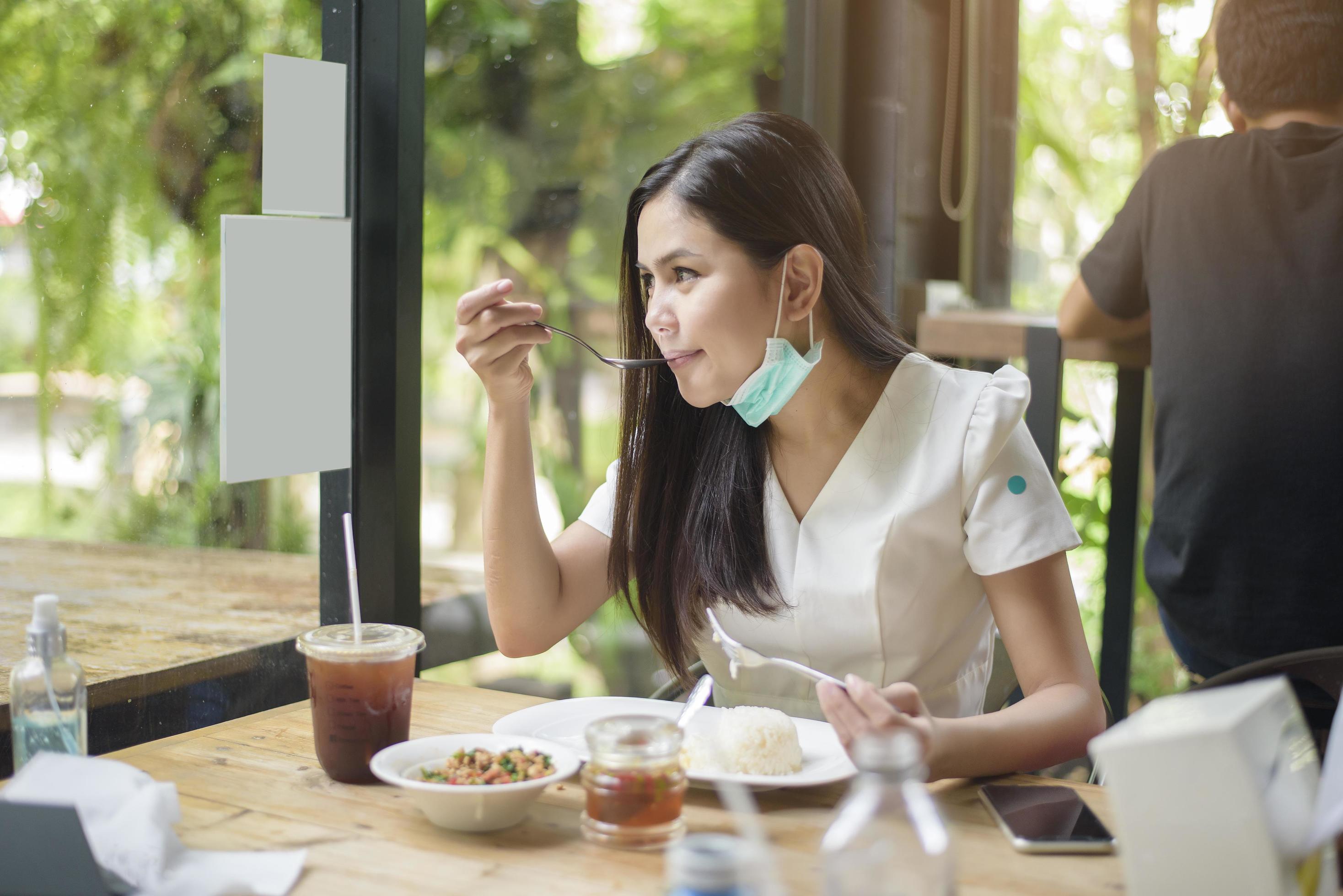 young woman with face mask is having food in restaurant, New normal concept. Stock Free