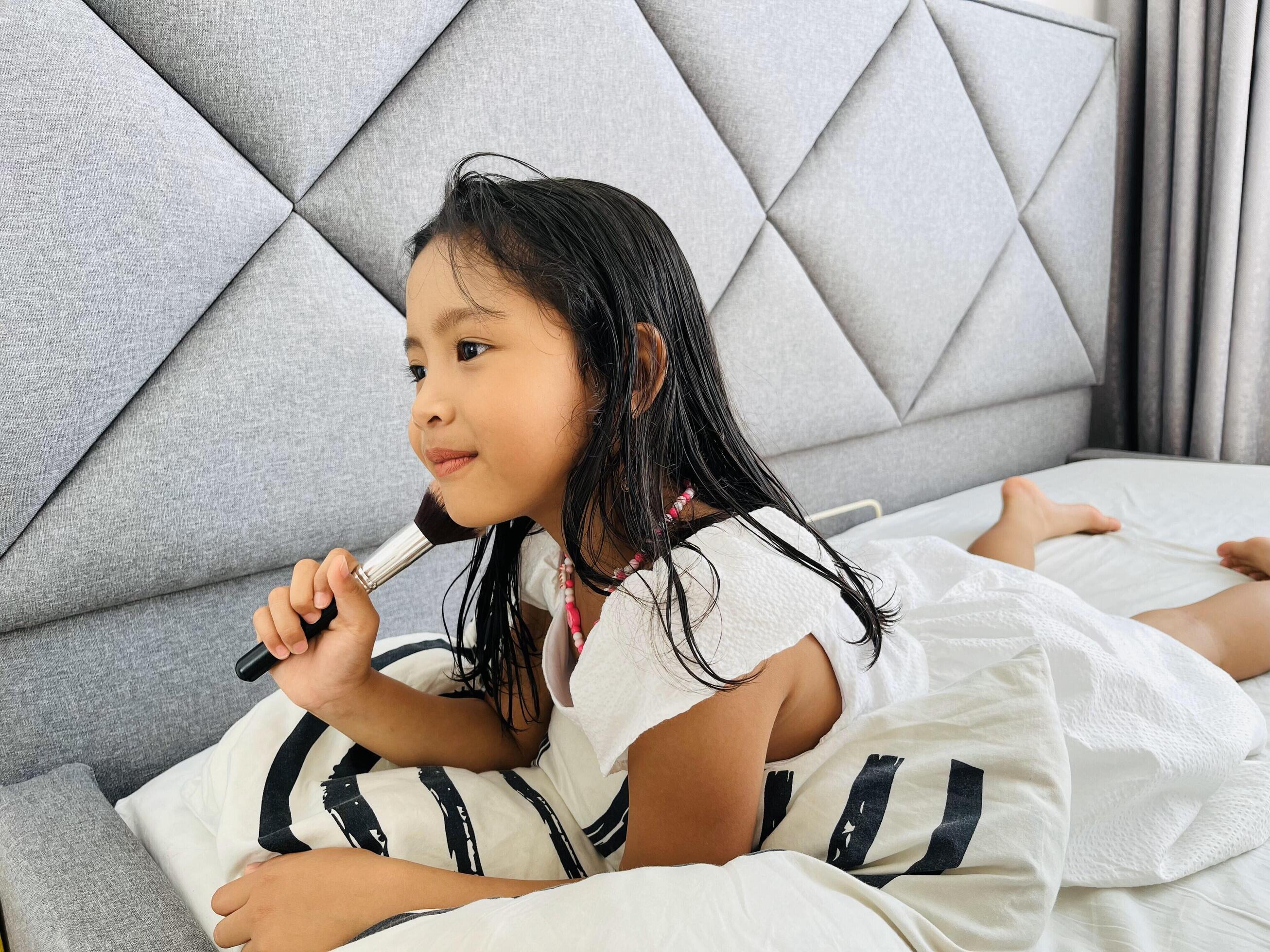 Beautiful little Asian girl holding blush brush. A five year old in beautiful white dresses preening in the bed Stock Free