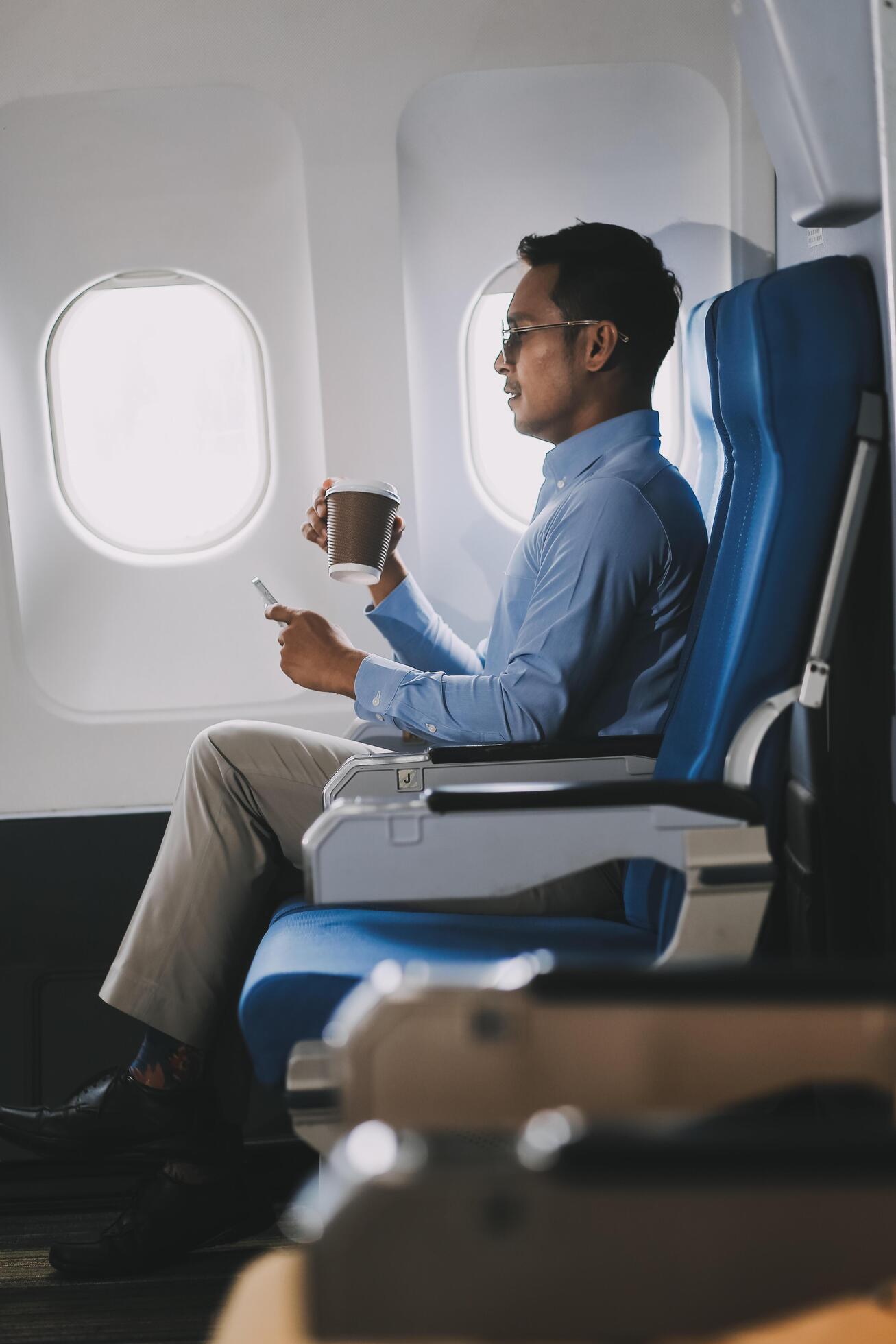 Asian businessman enjoying enjoys a coffee comfortable flight while sitting in the airplane cabin, Passengers near the window. Stock Free