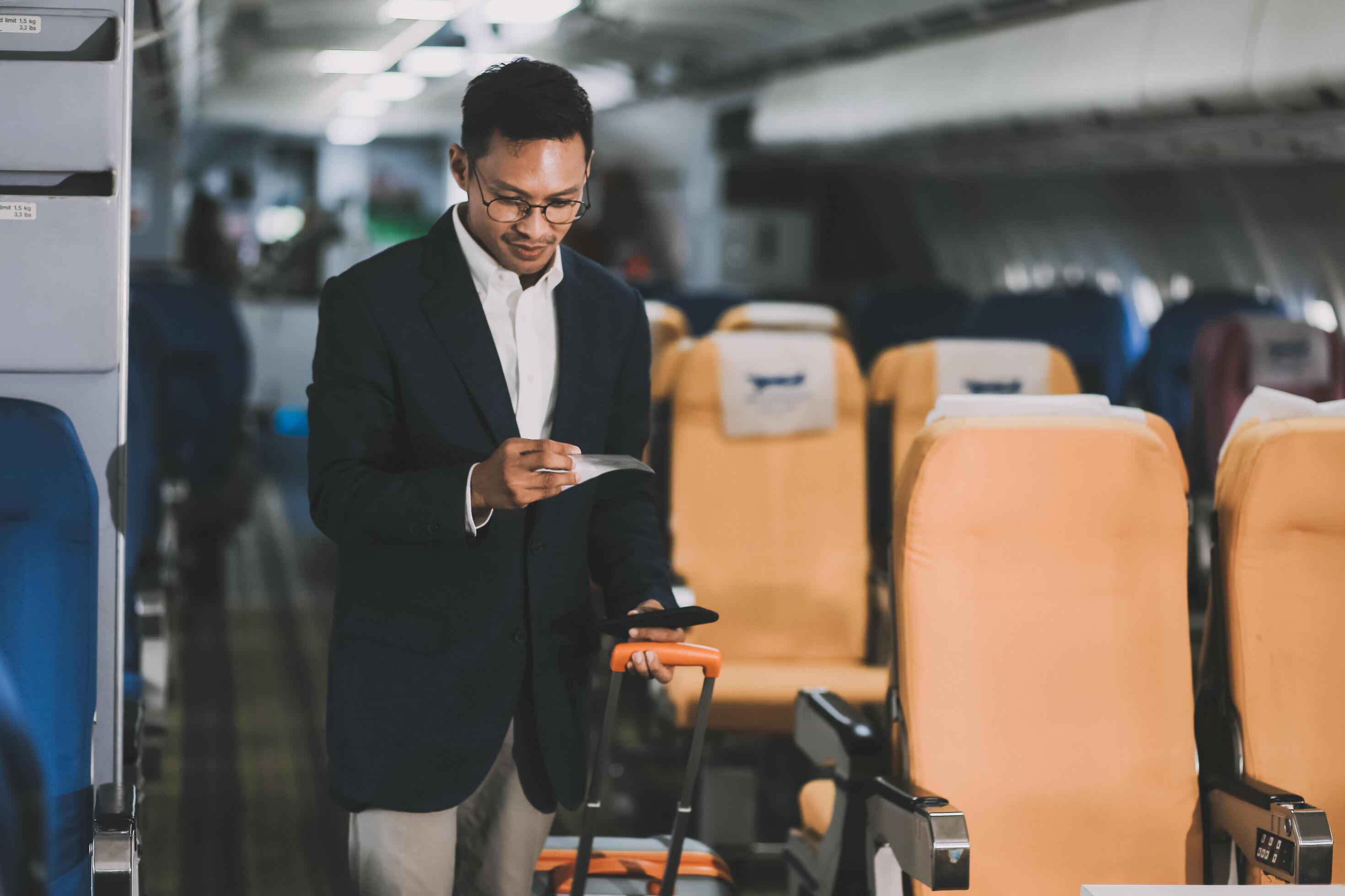 Handsome Asian male passenger takes his carry-on luggage out of the overhead locker after landing at his destination. transportation concept Stock Free