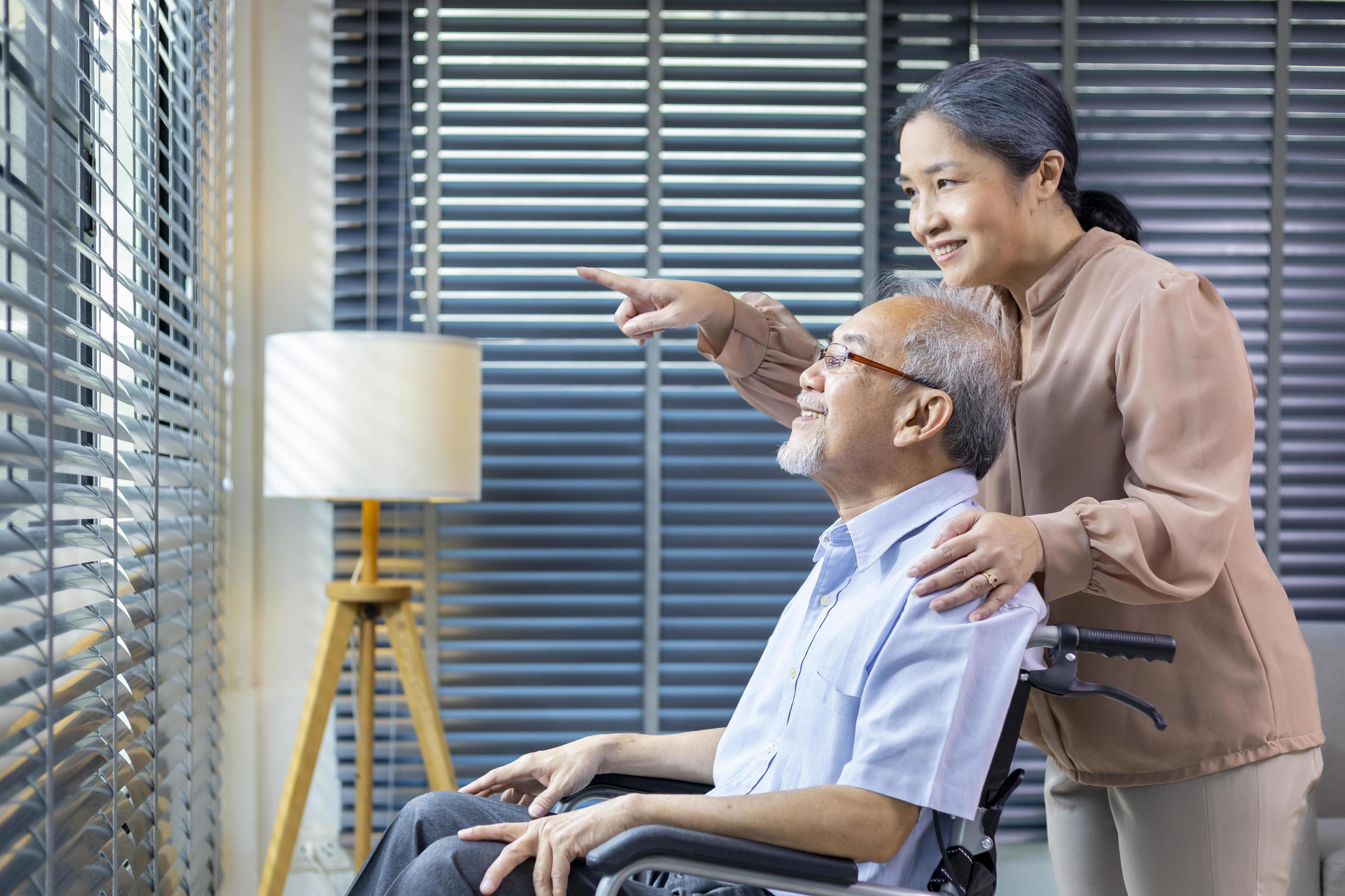 Asian senior man sitting in wheelchair at home with his wife is supporting and caring for love and retirement family concept Stock Free