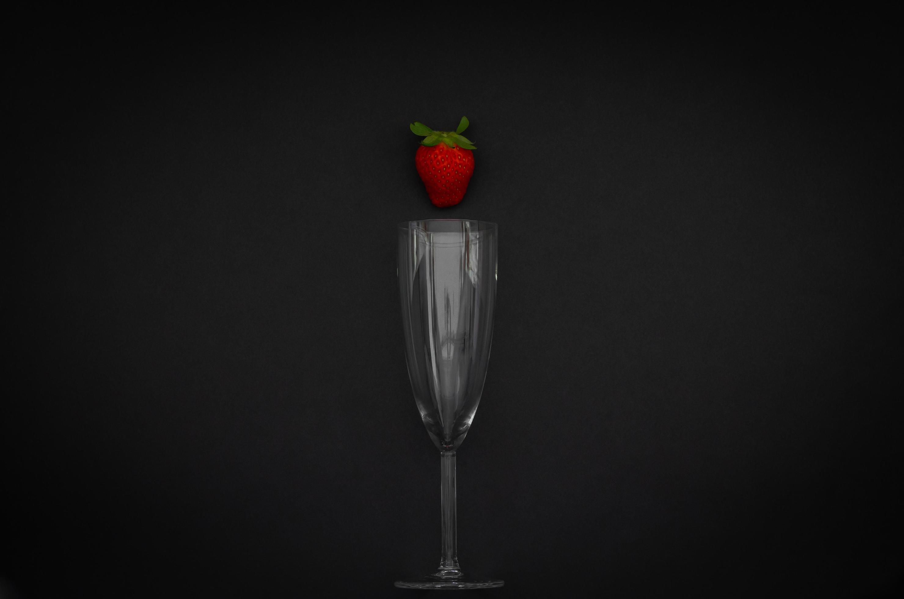 Strawberry and wineglass on dark background for minimalist flat lay black food and drink concept. Stock Free