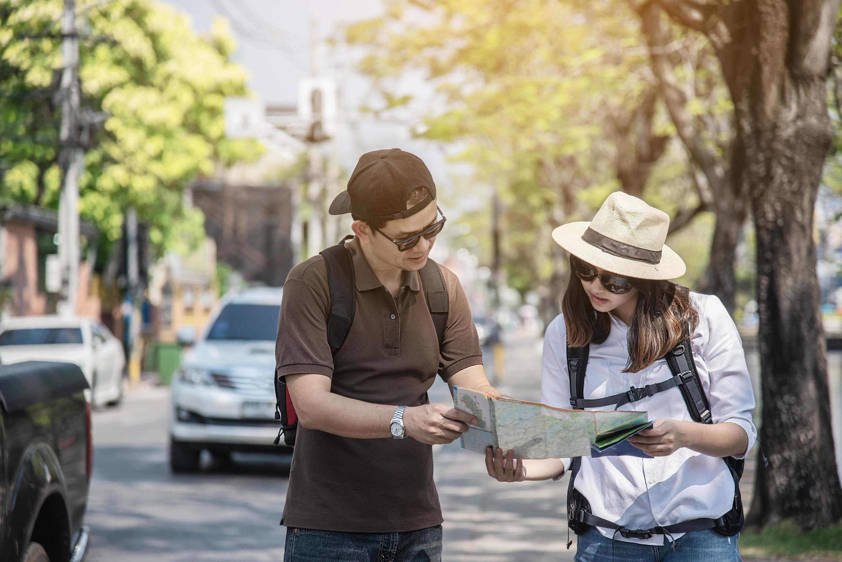 Asian backpack couple tourist holding city map crossing the road – travel people vacation lifestyle concept Stock Free