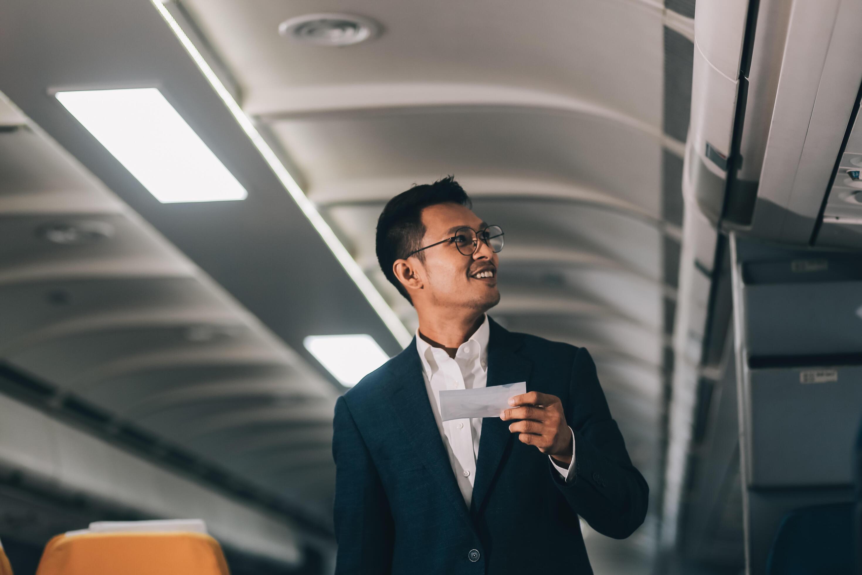 Handsome Asian male passenger takes his carry-on luggage out of the overhead locker after landing at his destination. transportation concept Stock Free