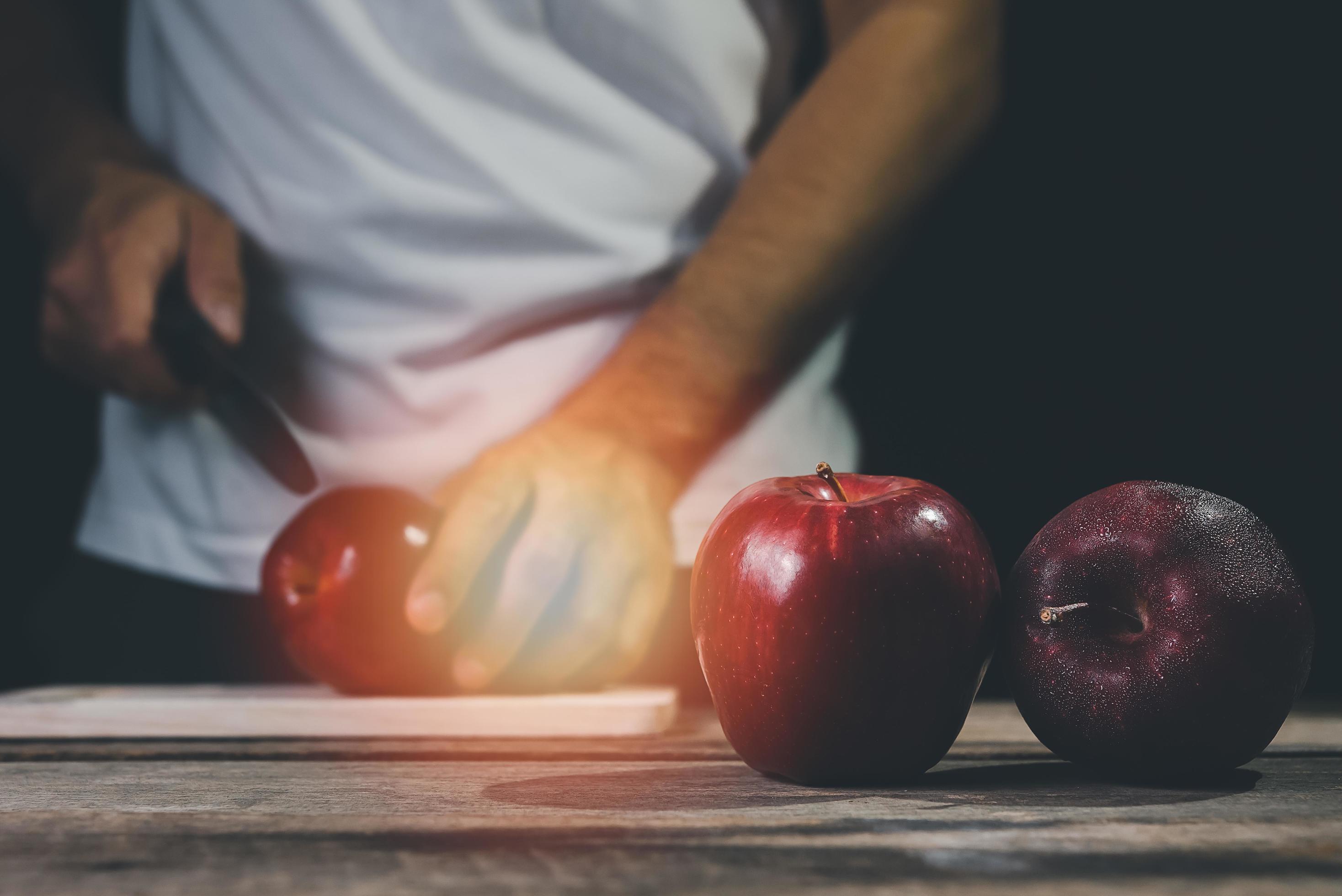 Man hand holding knife prepare to cut red apple on wood table and dark background. Fruits and food concept. Stock Free