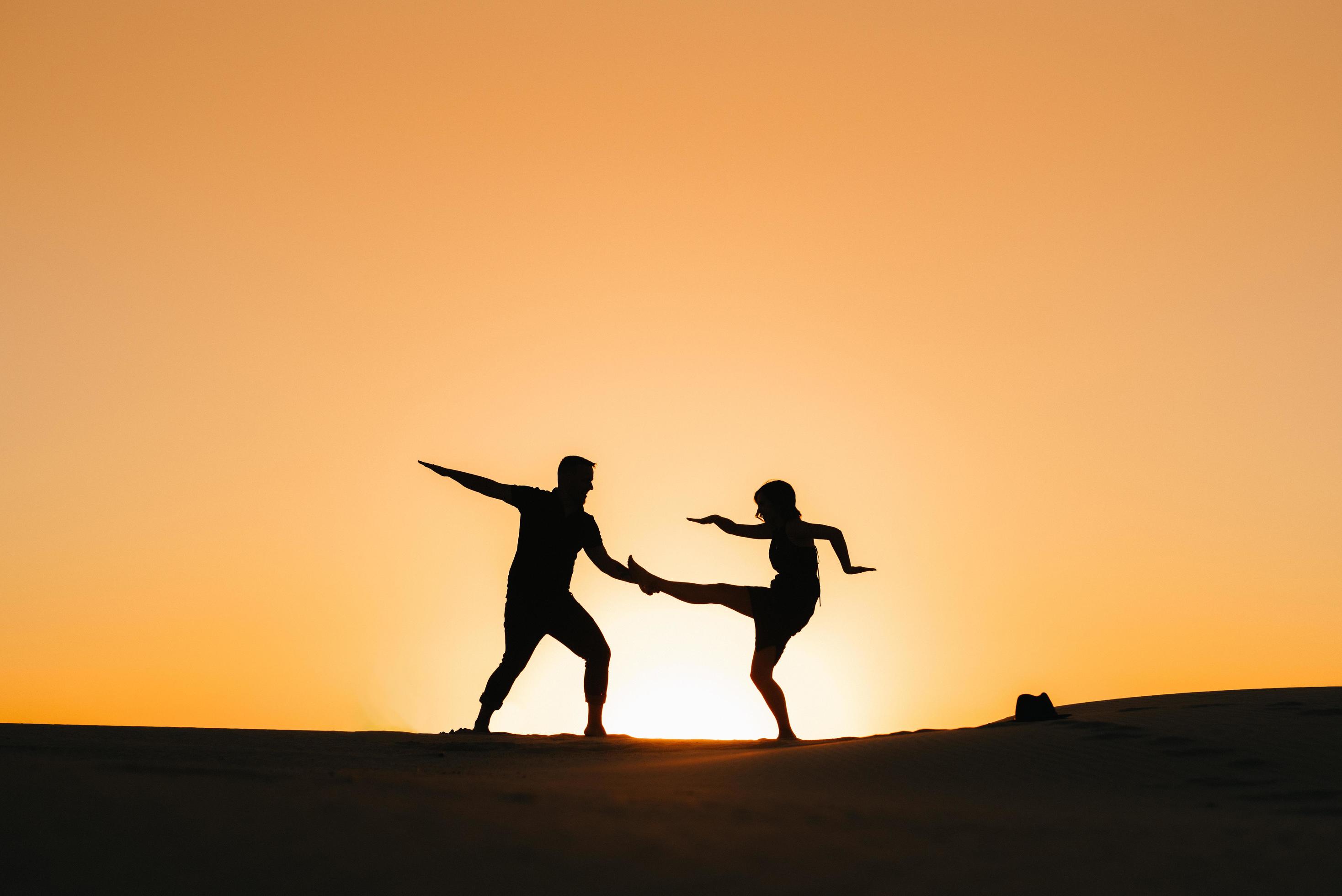 Silhouettes of a happy young couple on a background of orange sunset in the sand desert Stock Free