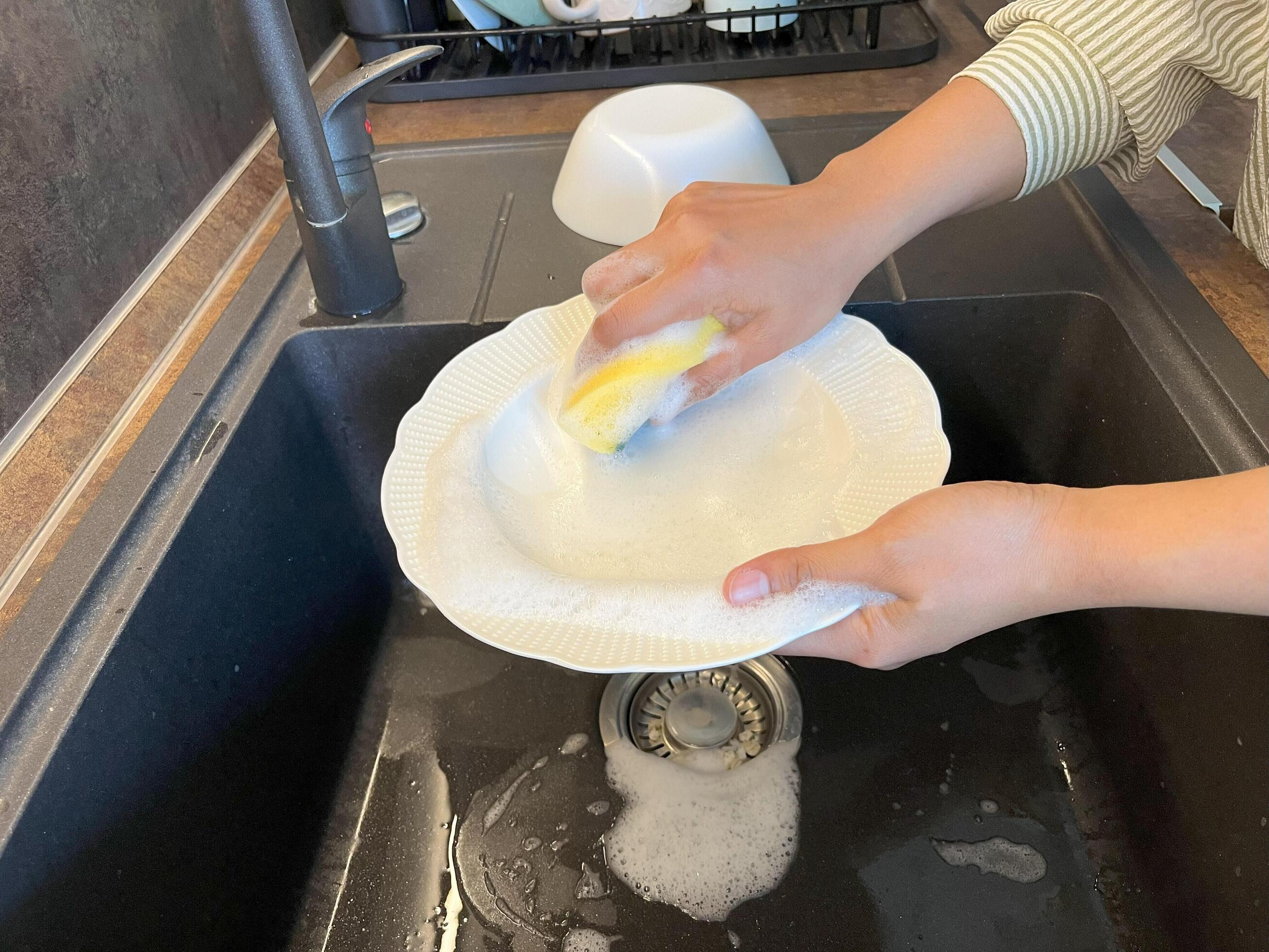 Close up of woman housewife is doing the dishes at home kitchen by using wash sponge and dishwashing soap. Clean the plate Stock Free