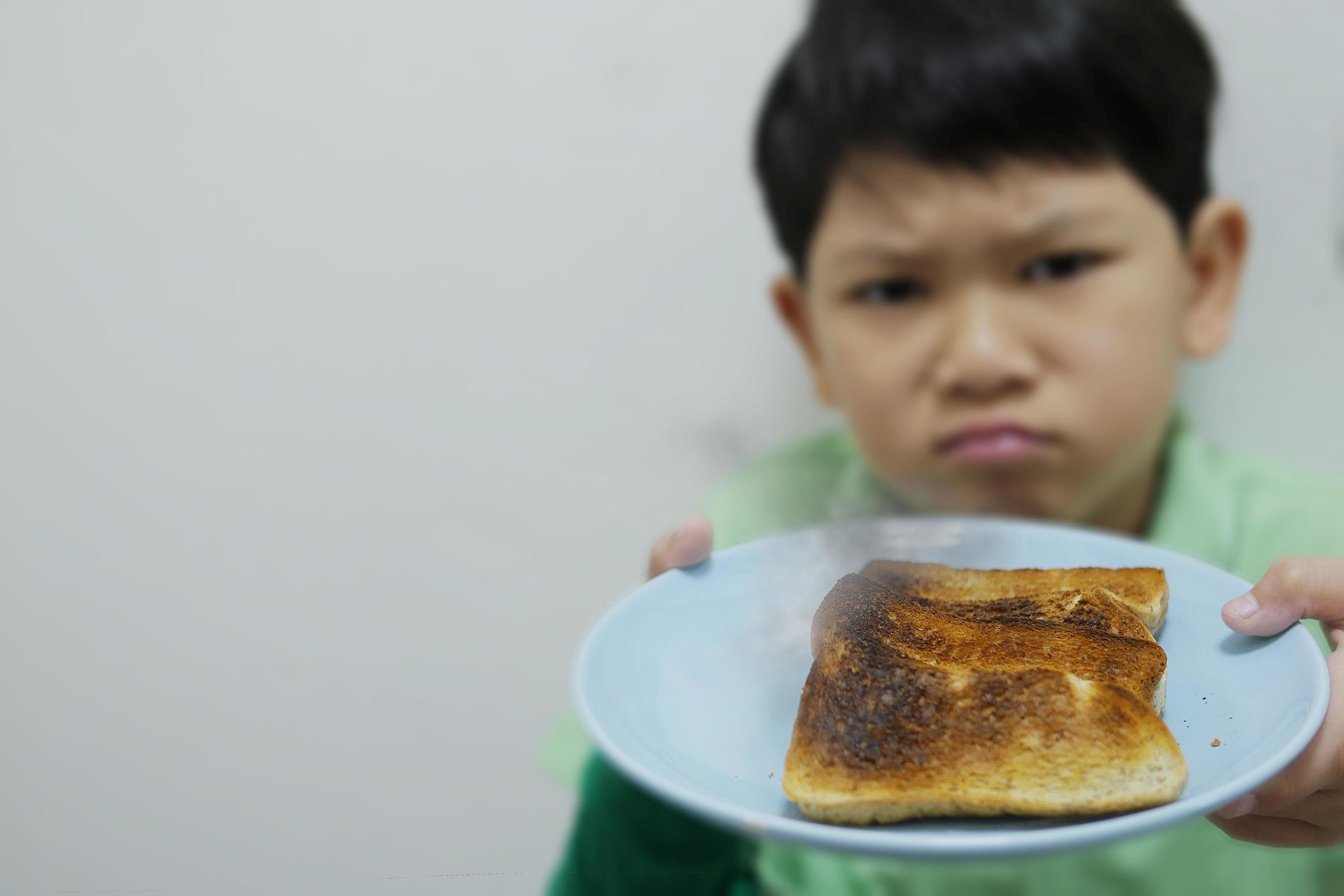 asian boy show over roasted burnt grilled bread dish with bad unhappy mood face – food breakfast disappoint concept Stock Free