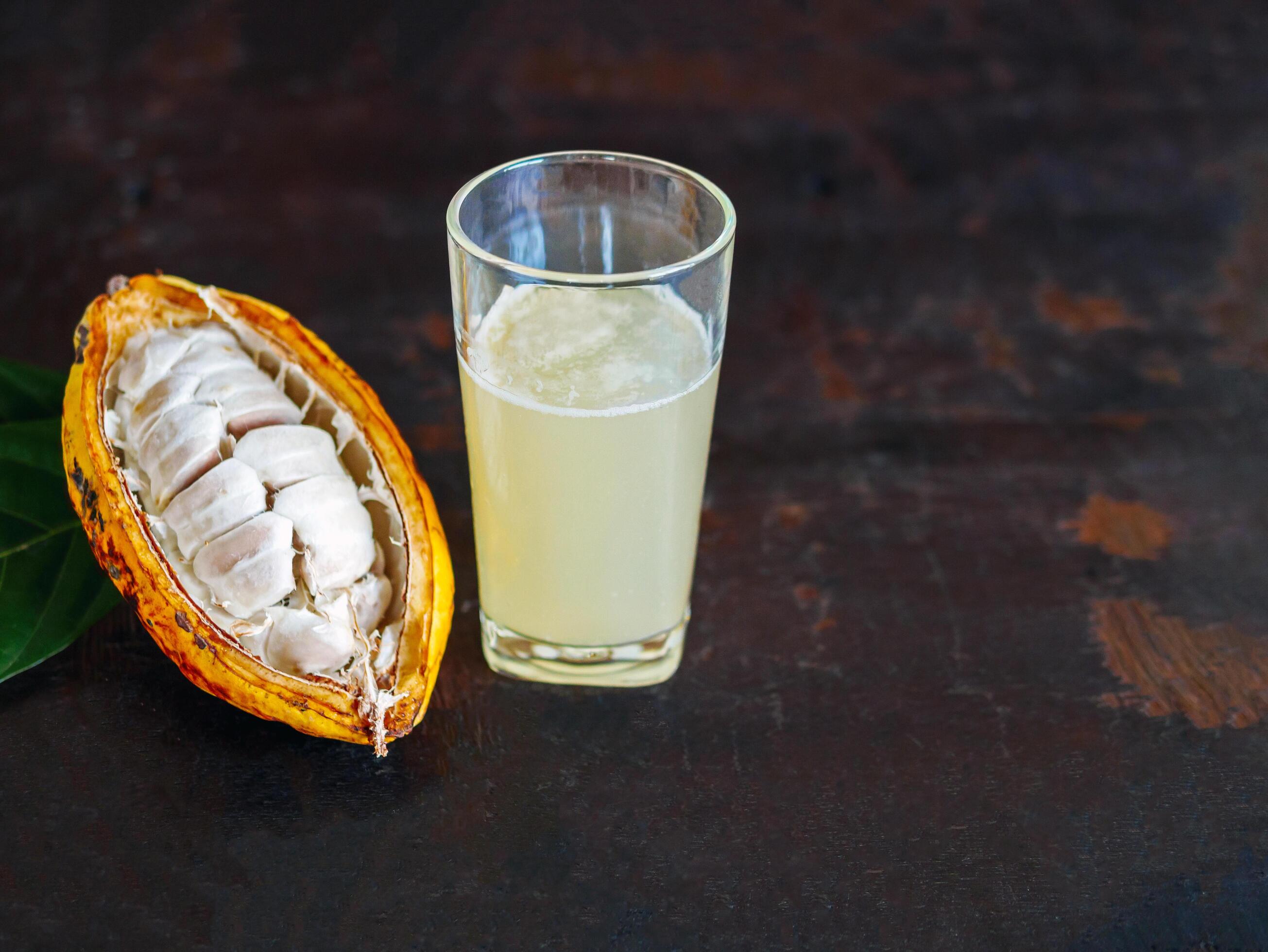 Fresh cacao water in glass and half sliced ripe yellow cacao pod with white cocoa seed, Cacao juice in glass on vintage wooden background Stock Free