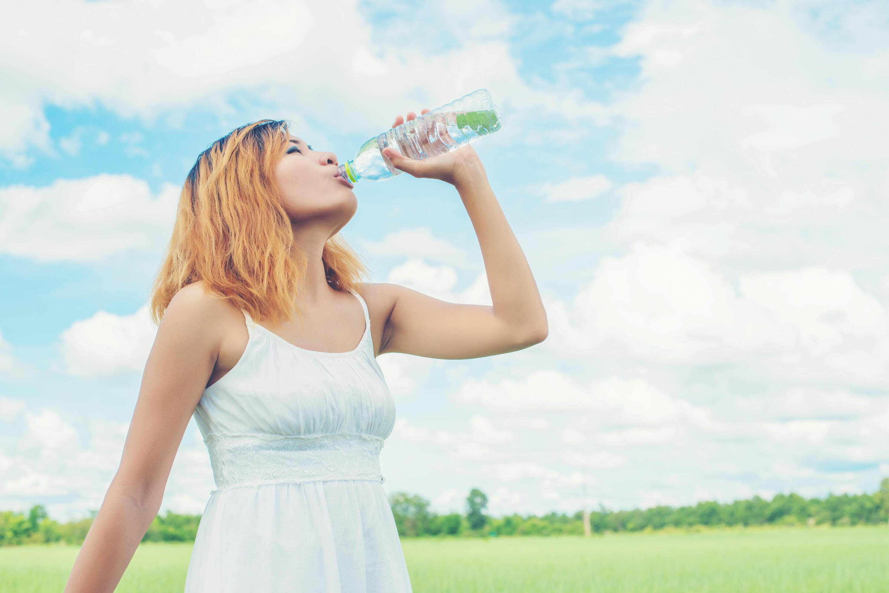 Women lifestyle concept young beautiful woman with white dress drinking water at summer green park. Stock Free