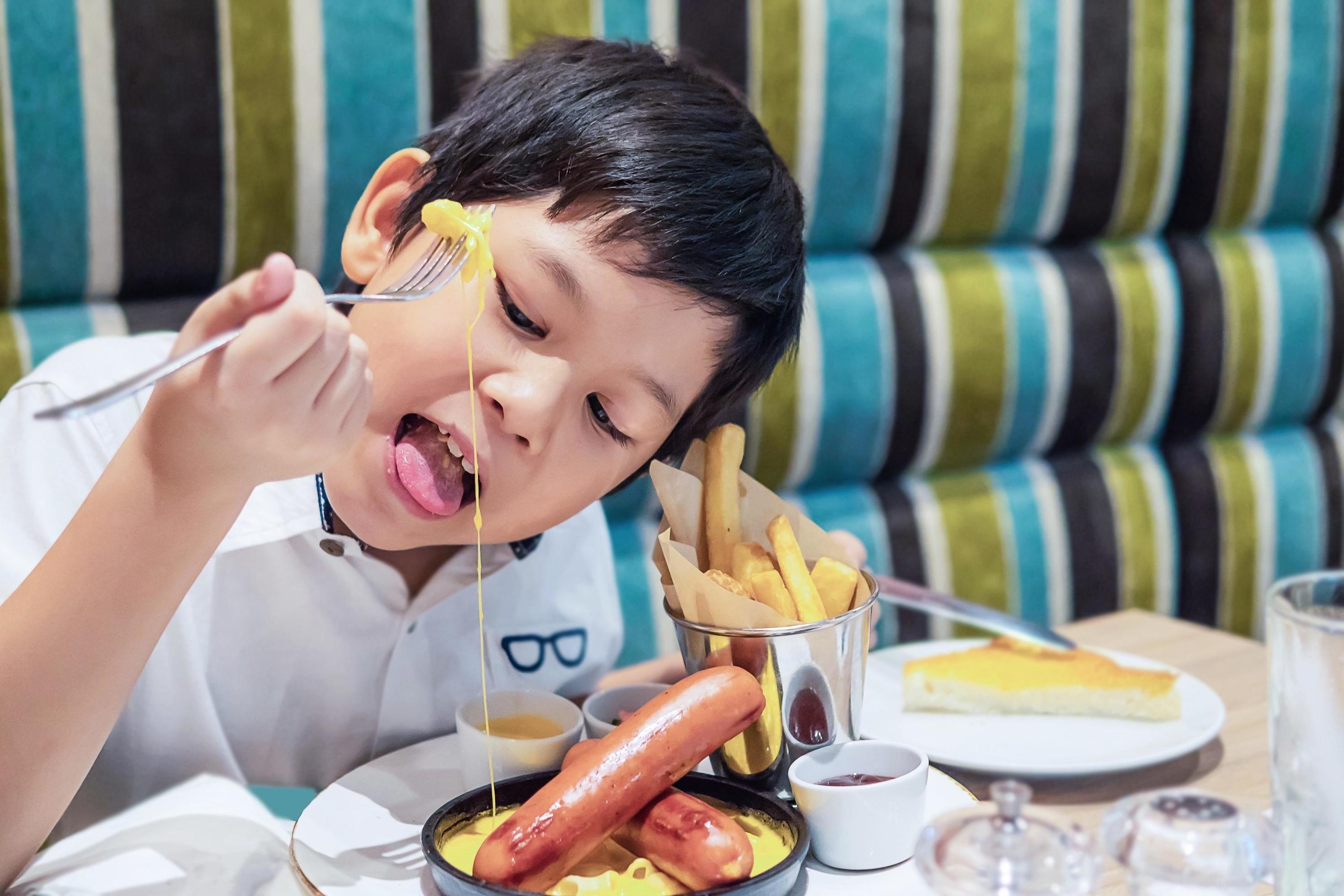 Asian boy eating French fries happily – child with unhealthy junk food concept Stock Free