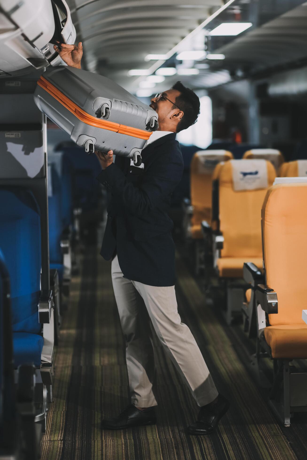 Handsome Asian male passenger takes his carry-on luggage out of the overhead locker after landing at his destination. transportation concept Stock Free