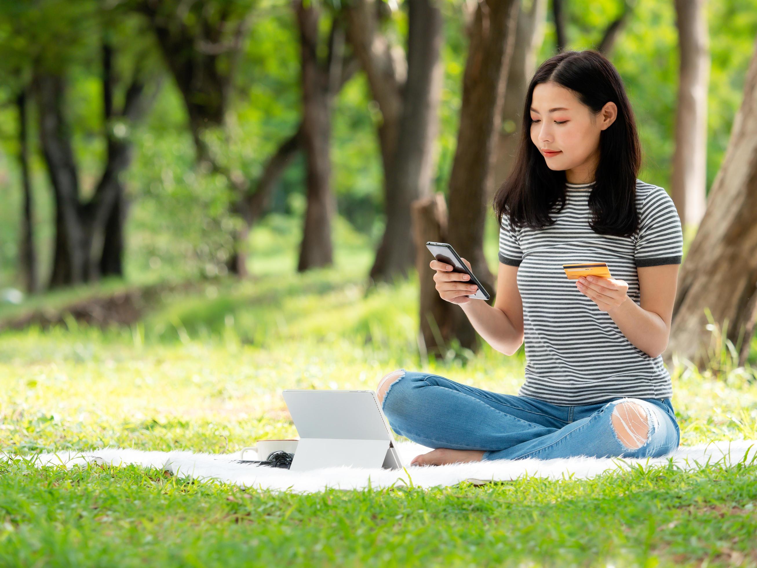 A beautiful Asian woman is happy as she uses her credit card to make purchases online via smartphone Stock Free