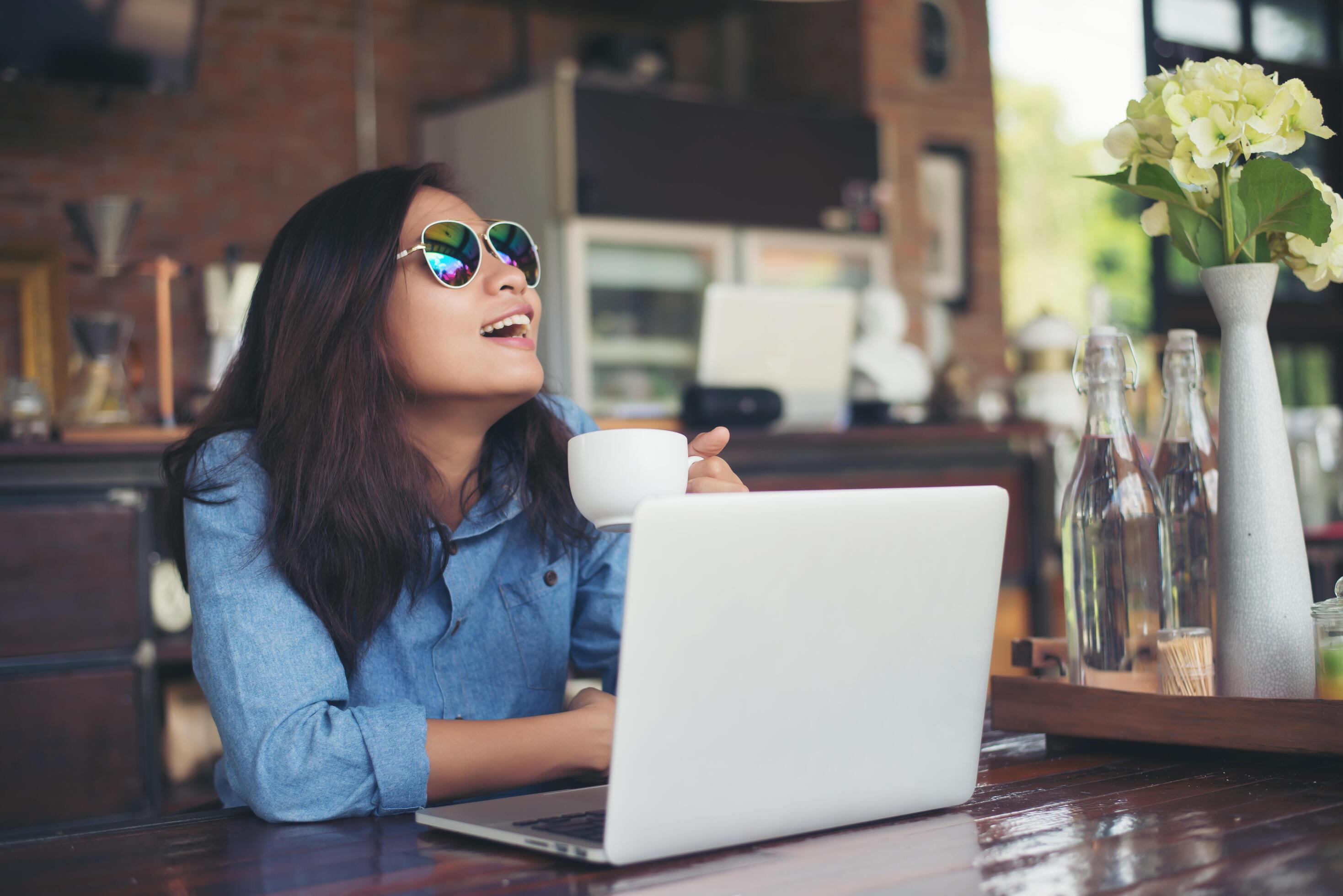 Pretty young hipster woman sitting in a cafe with her laptop, looked away and smiled happy, Relaxing with holiday, Woman lifestyle concept. Stock Free