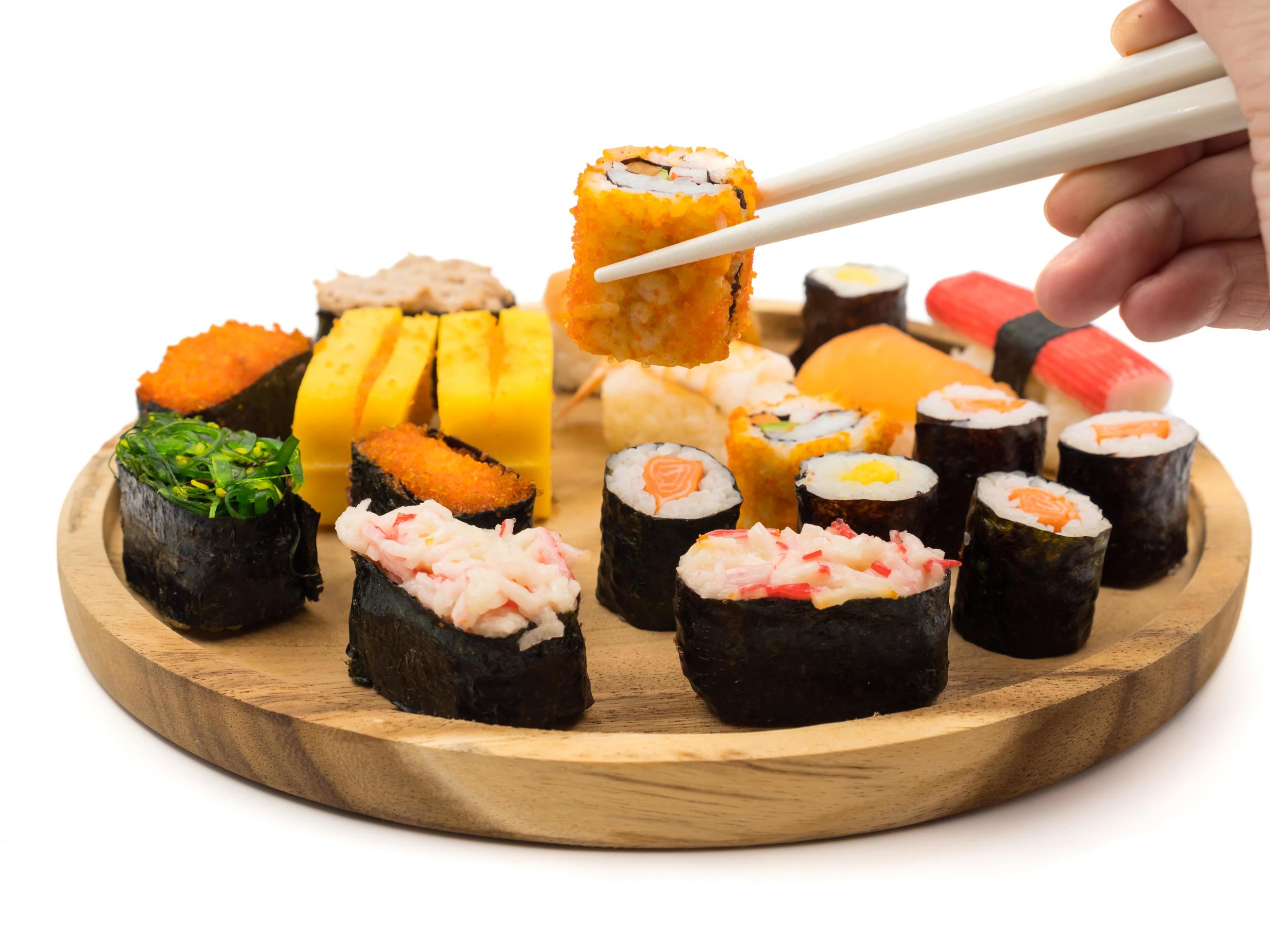 Hand holding sushi roll with chopsticks, Sushi set on wooden plate on white background, Japanese food. Stock Free