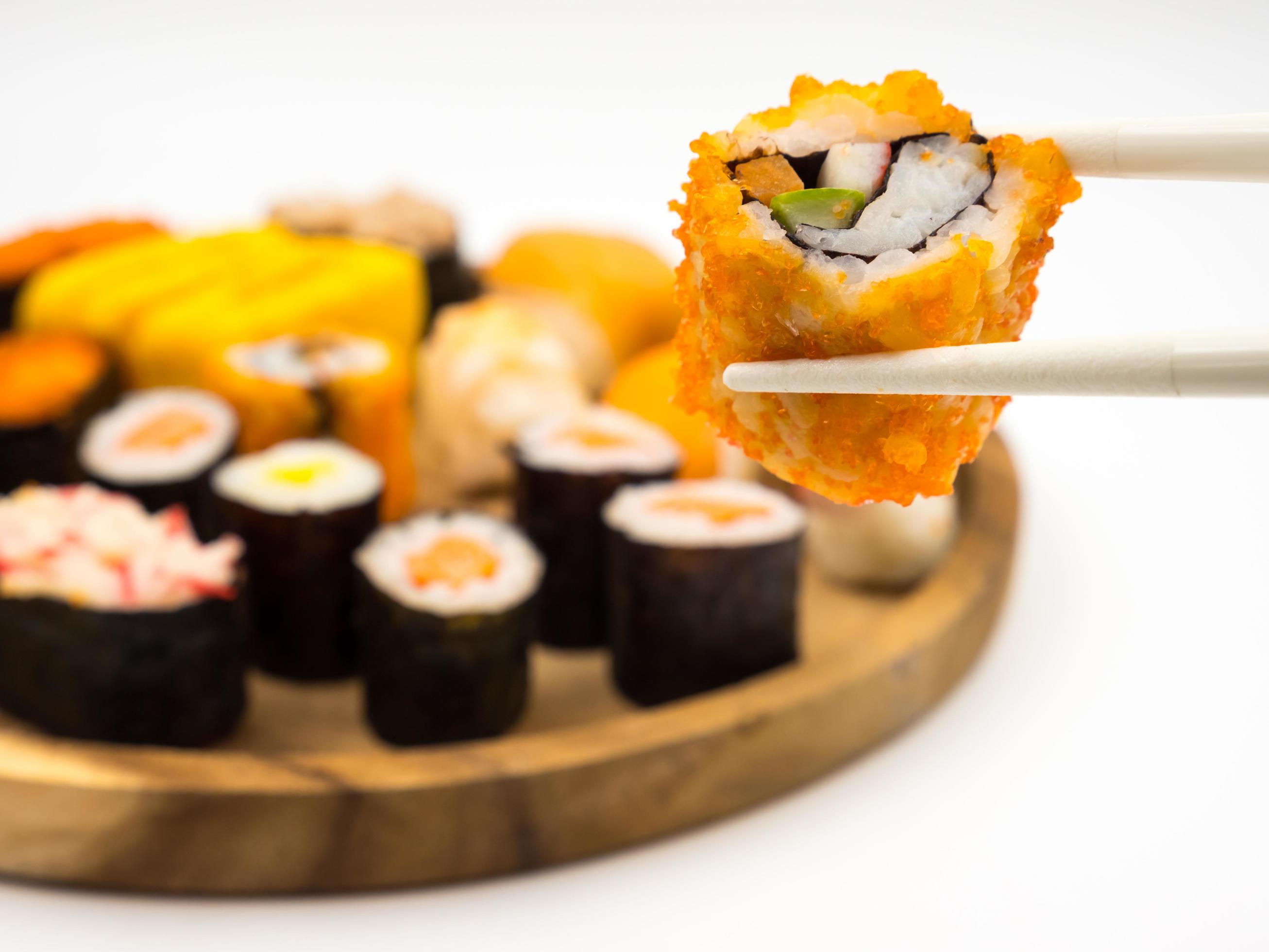 Hand holding sushi roll with chopsticks, Sushi set on wooden plate background, Japanese food. Stock Free