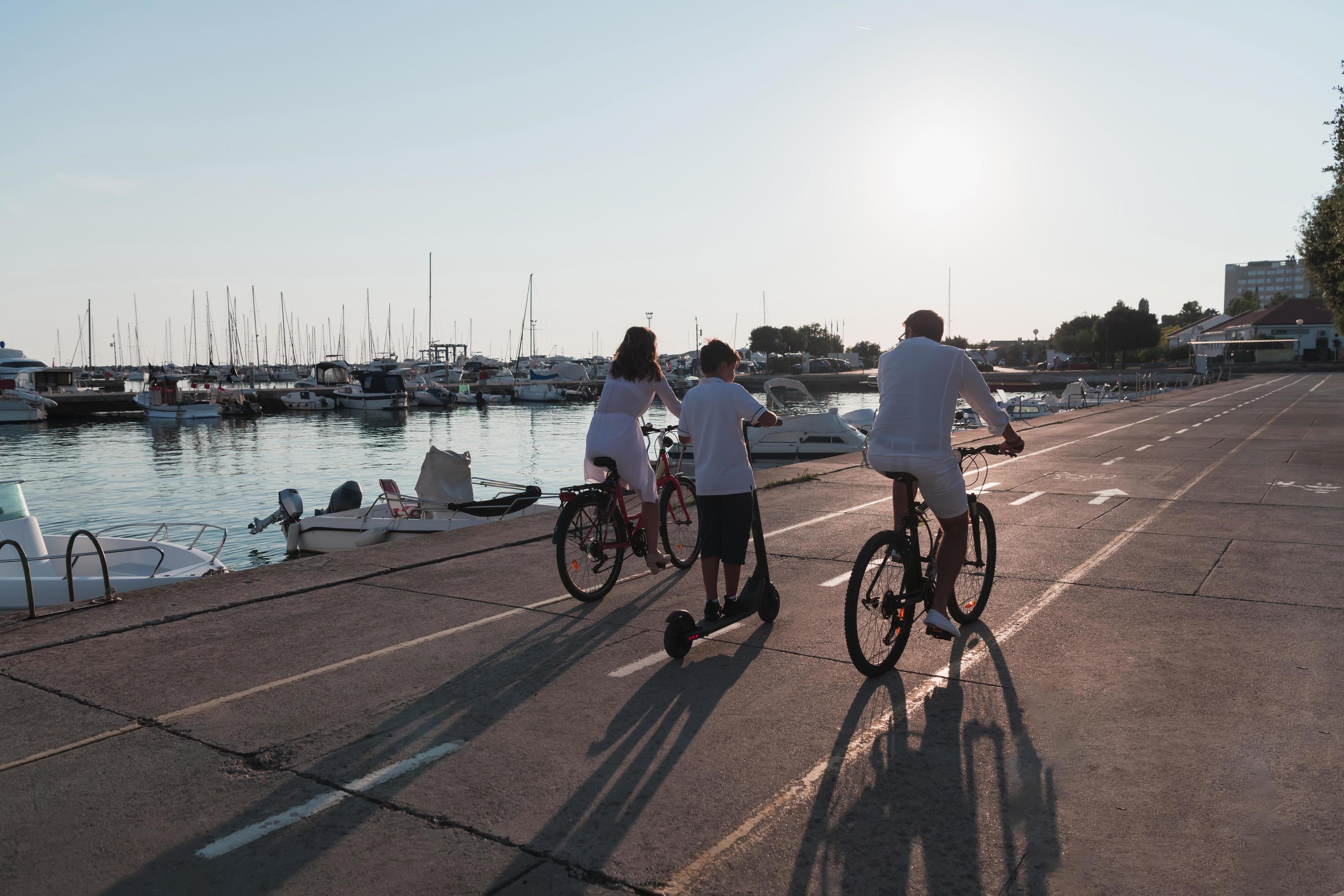 Happy family enjoying a beautiful morning by the sea together, parents riding a bike and their son riding an electric scooter. Selective focus Stock Free