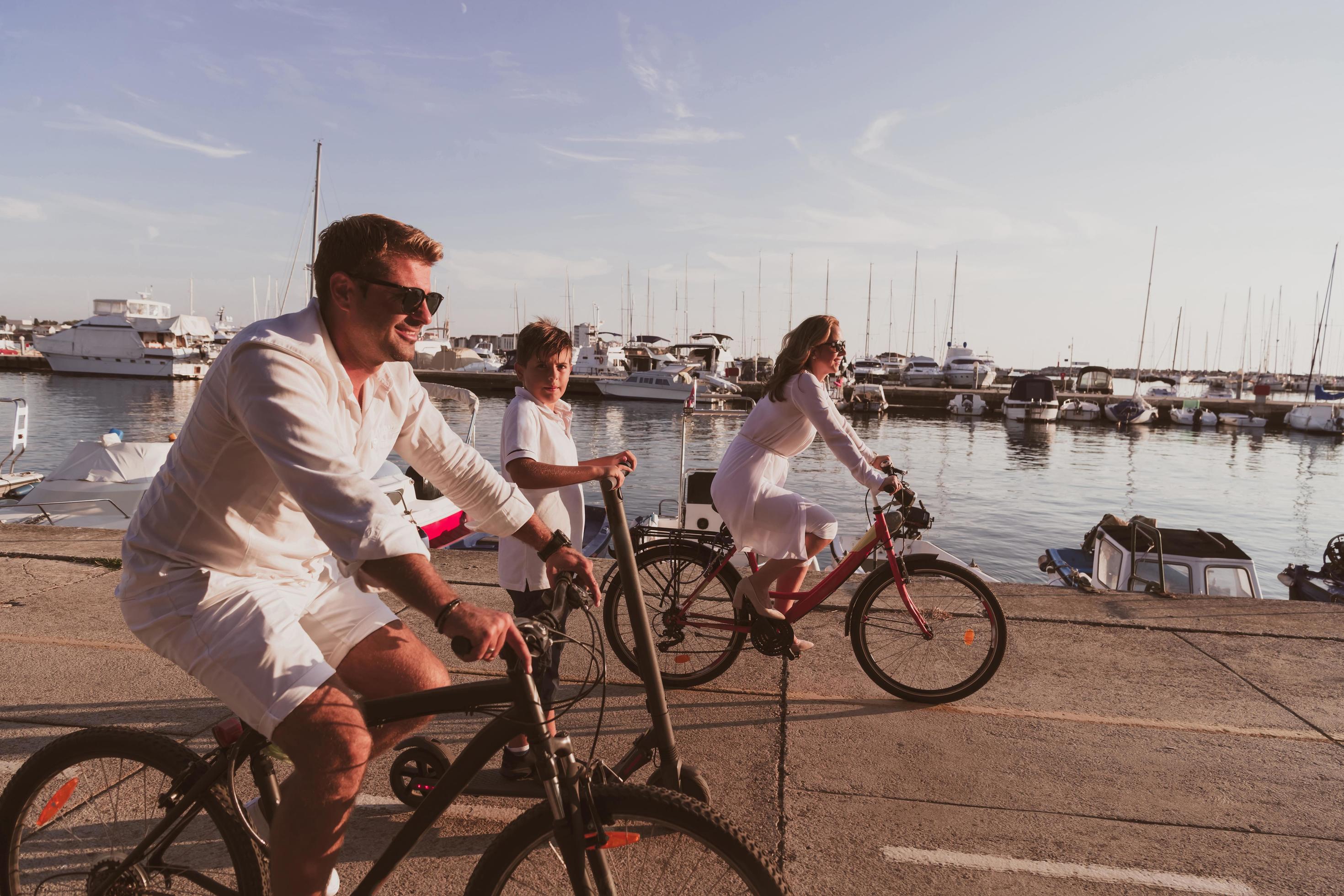 Happy family enjoying a beautiful morning by the sea together, parents riding a bike and their son riding an electric scooter. Selective focus Stock Free