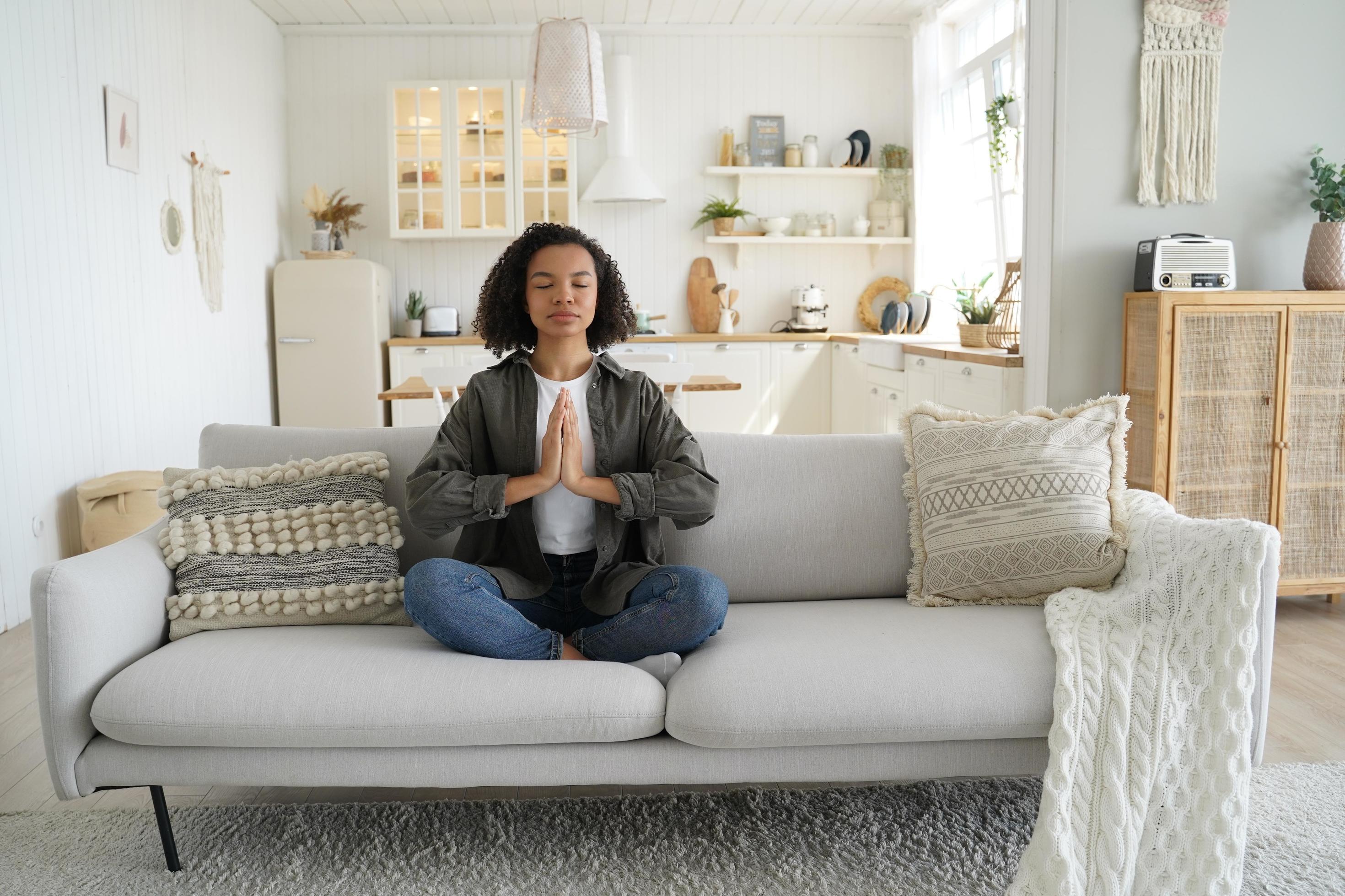 Mixed race girl practices yoga, meditation at home sitting in lotus pose on couch. Healthy lifestyle Stock Free