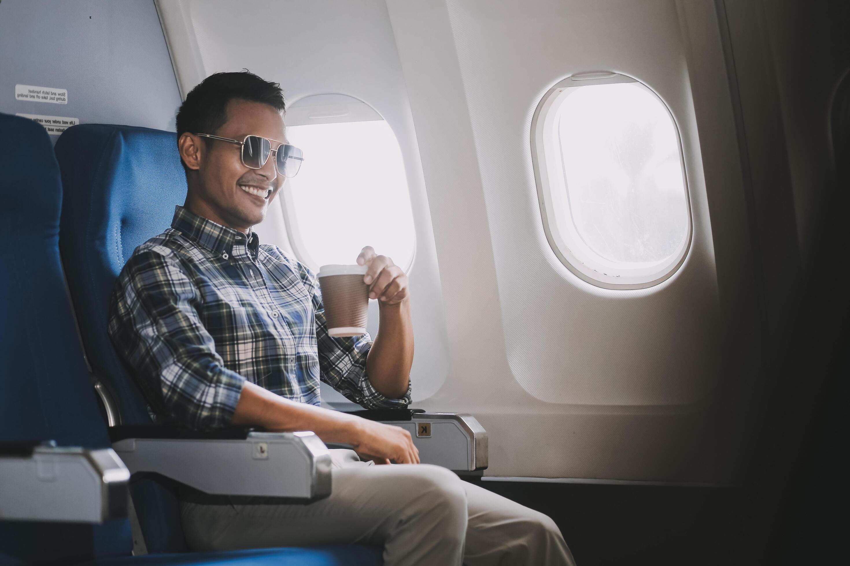 Asian man enjoying enjoys a coffee comfortable flight while sitting in the airplane cabin, Passengers near the window. Stock Free