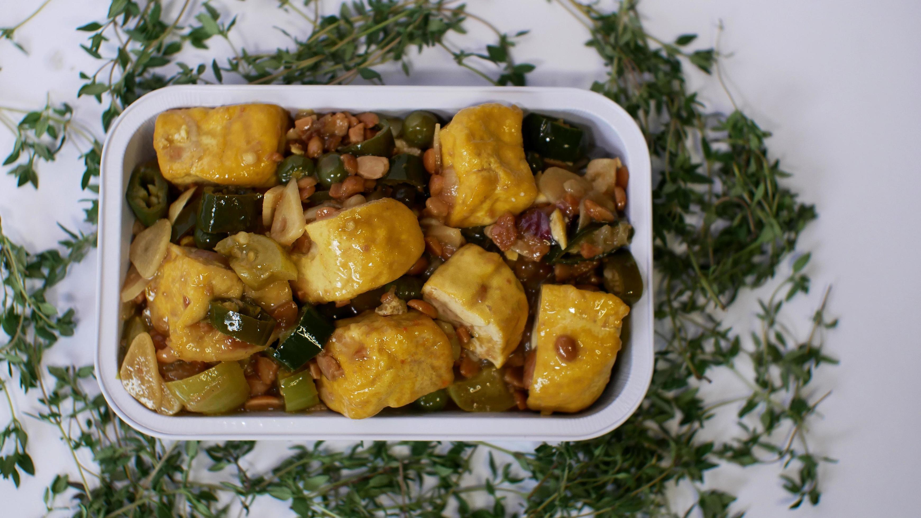 Vegetable tofu with yellow spices Indonesian food served in an aluminum holder with a white background with a few green leaves around it Stock Free