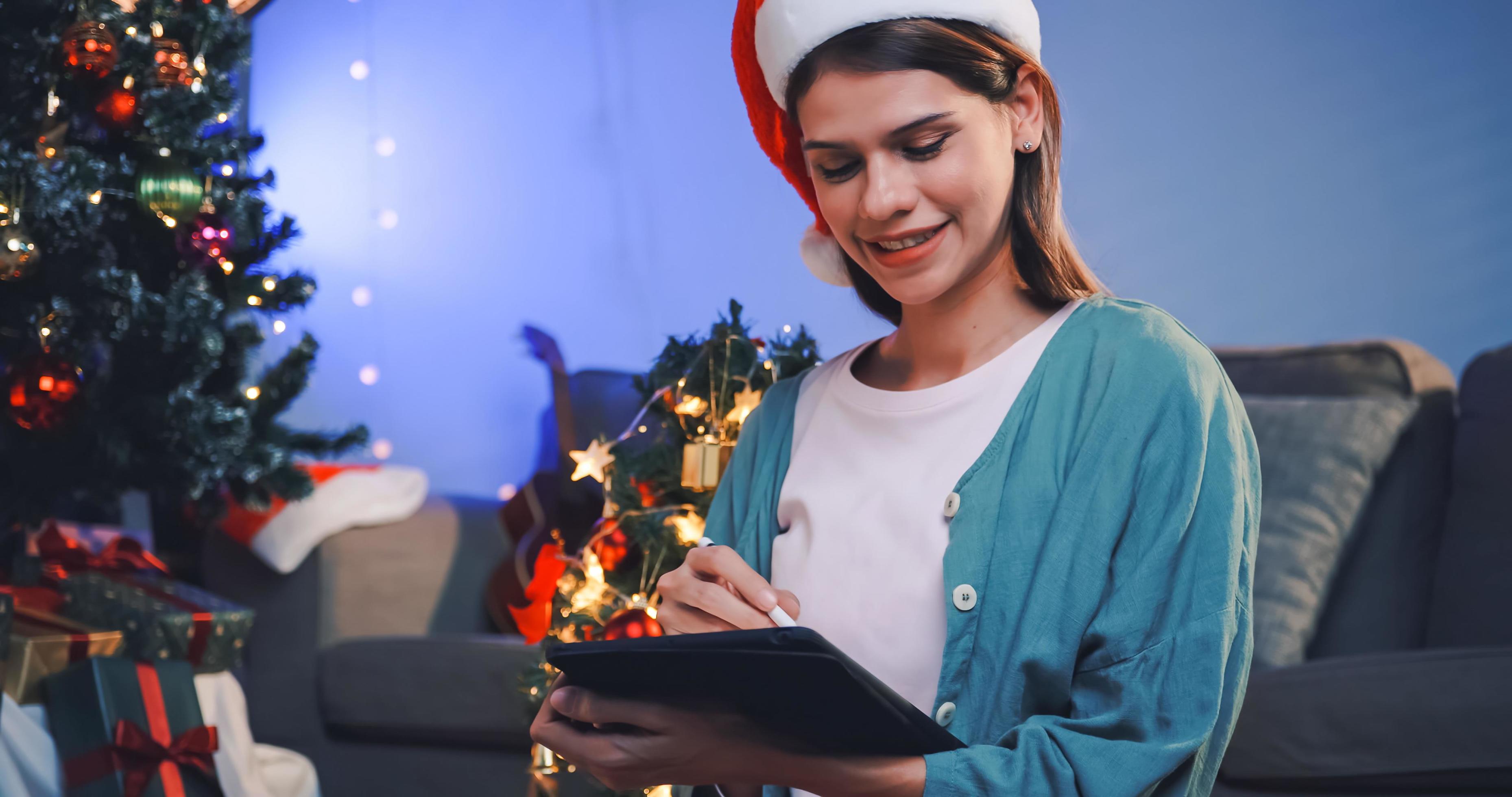 A beautiful woman is using a tablet computer to design Christmas cards for her family and friends. Stock Free