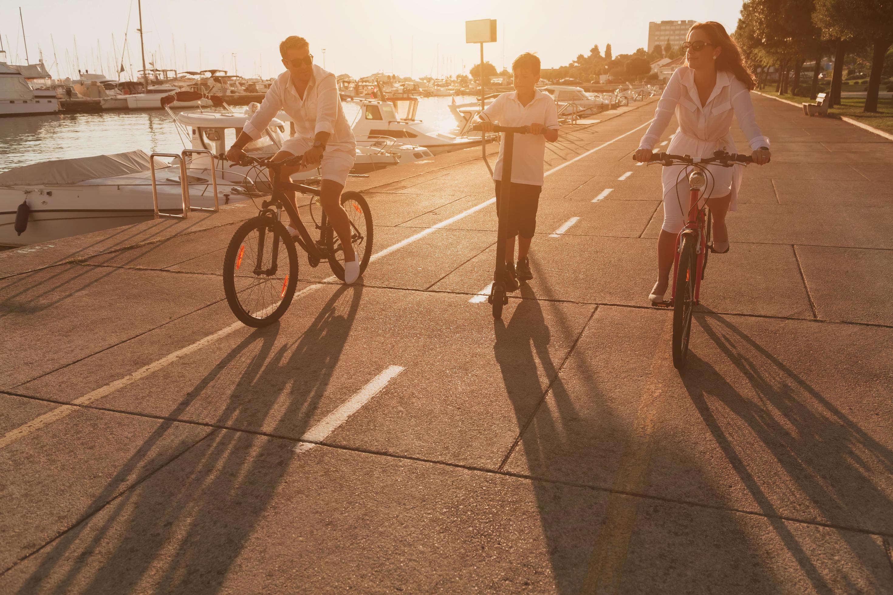 Happy family enjoying a beautiful morning by the sea together, parents riding a bike and their son riding an electric scooter. Selective focus Stock Free