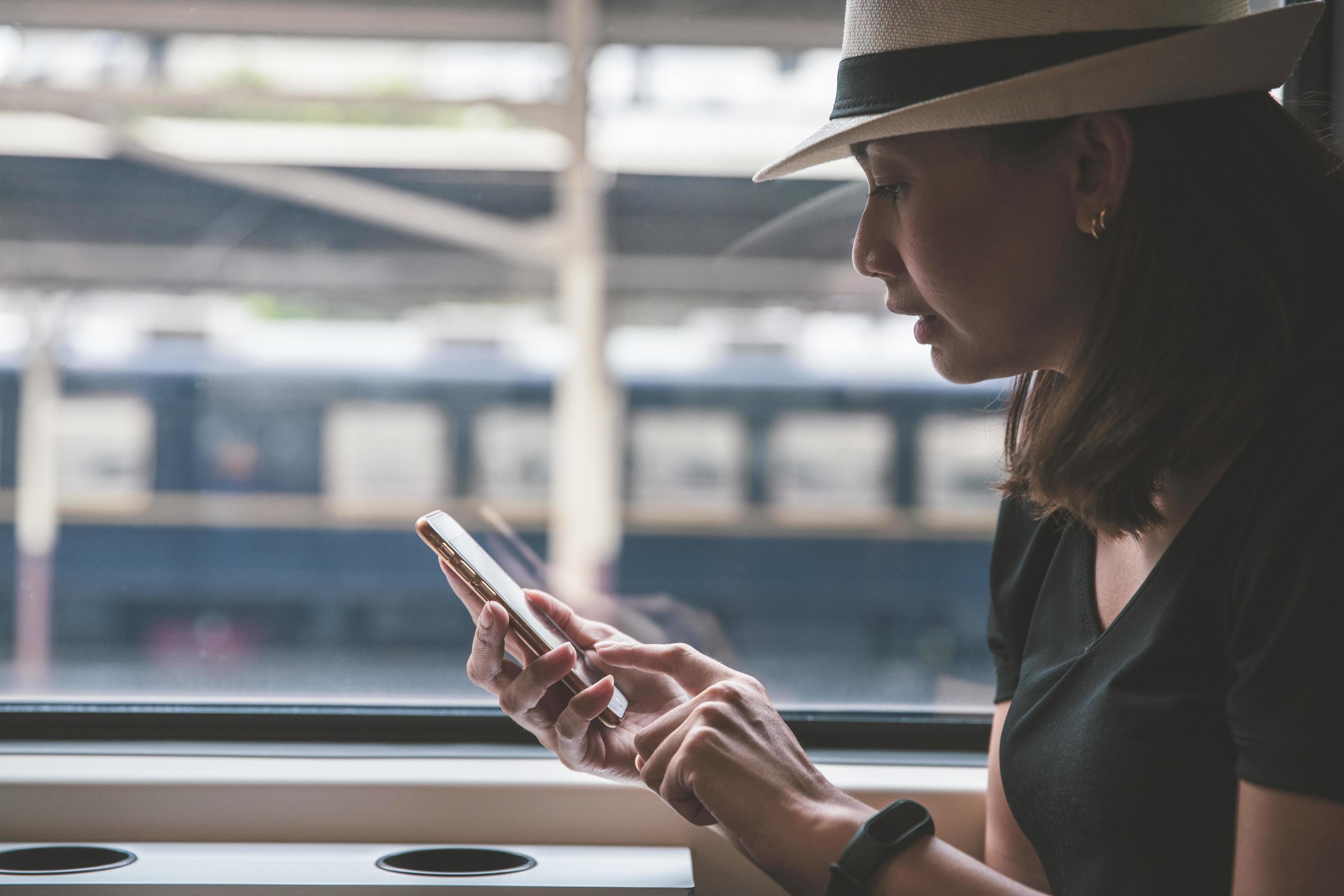 Beautiful young woman traveler using smartphone at a train station, transportation and travel lifestyle concept Stock Free