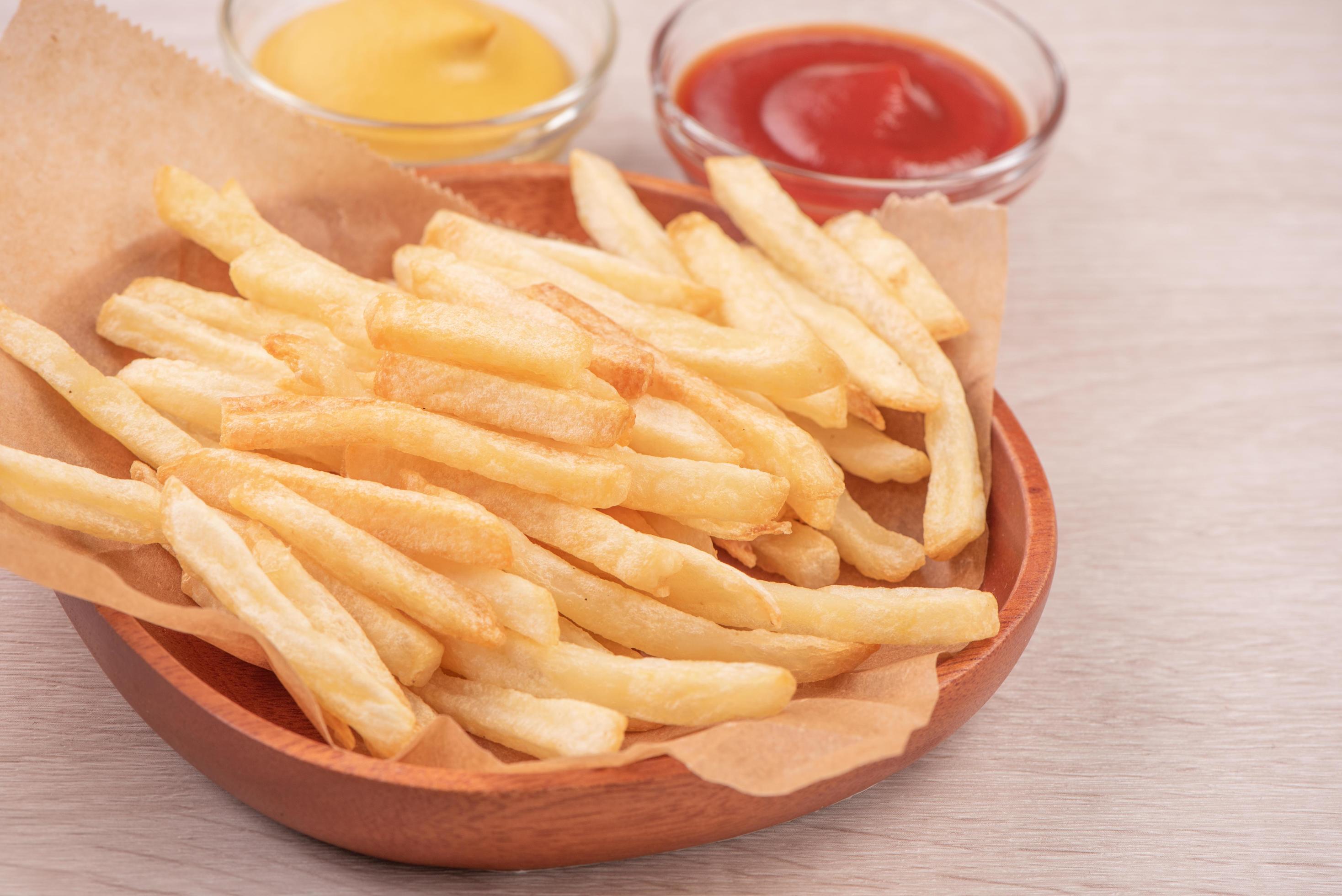 Golden yummy deep French fries on kraft baking sheet paper and serving tray to eat with ketchup and yellow mustard, close up, lifestyle. Stock Free