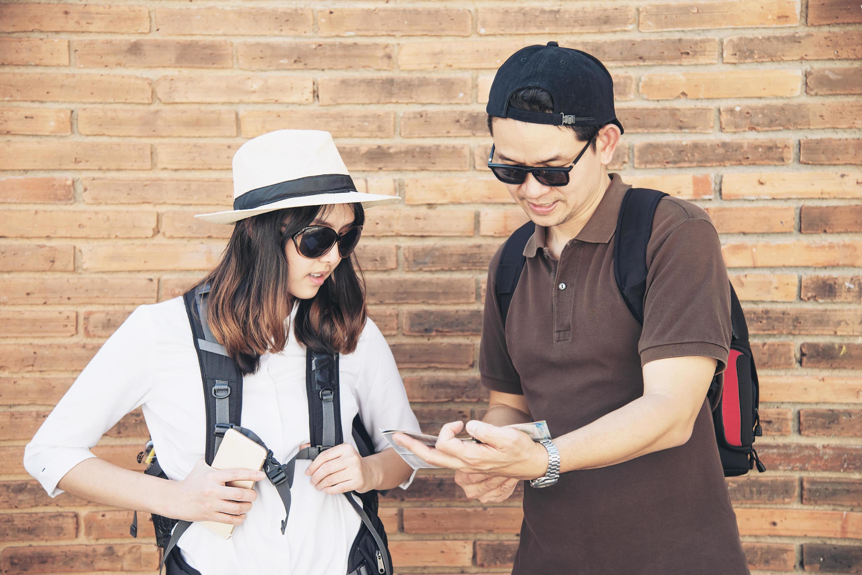 Asian backpack couple tourist holding city map crossing the road – travel people vacation lifestyle concept Stock Free