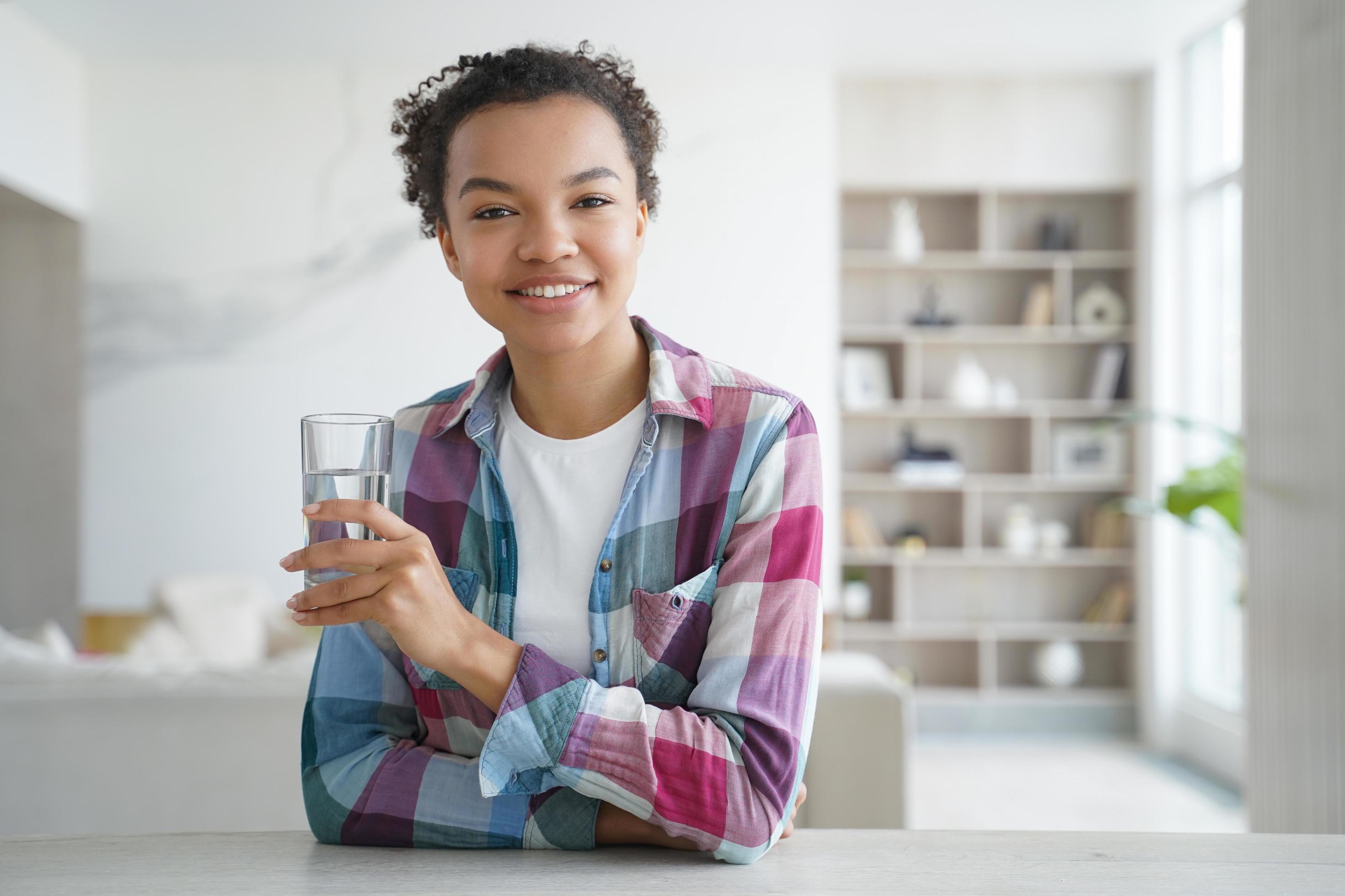 Happy african american girl drinks water from a glass. Healthy lifestyle, morning health routine. Stock Free