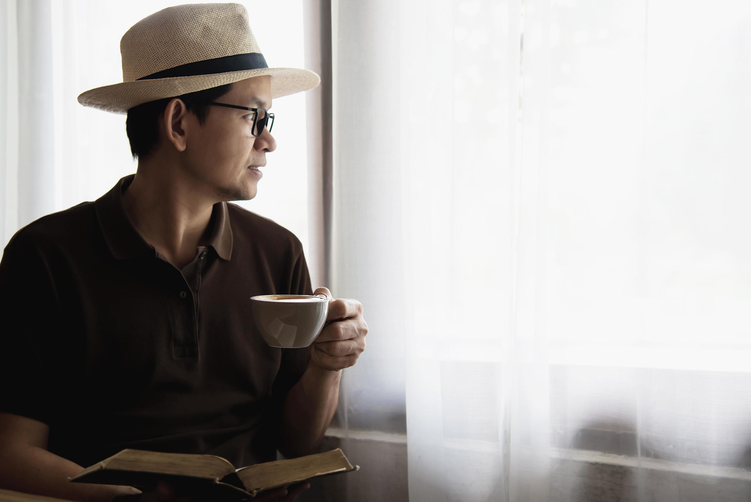 Relax Asian man drink coffee and read book in a modern style coffee shop – people with coffee cup easy lifestyle concept Stock Free