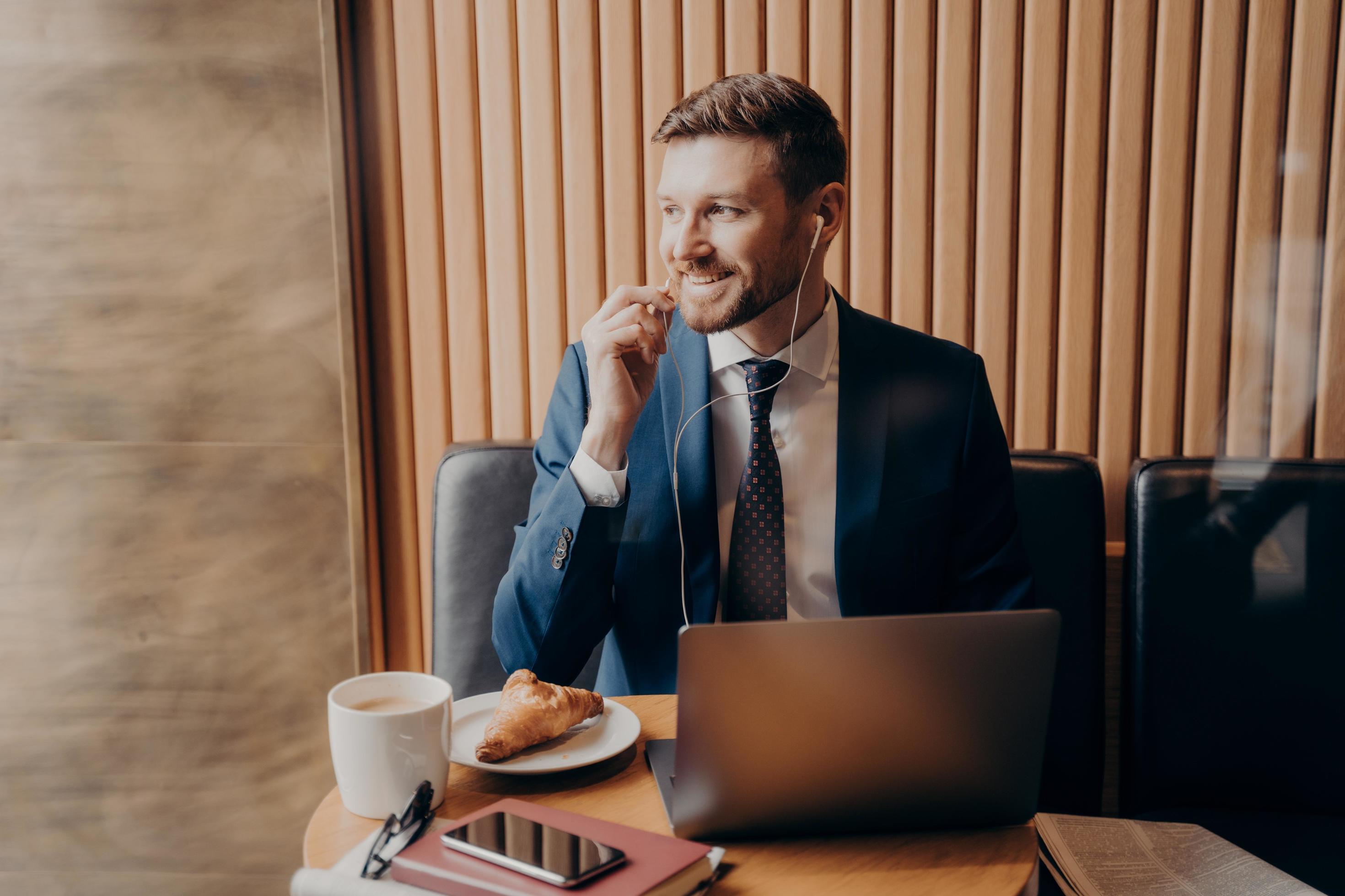 Male investor in blue suit talking with business partner online through laptop in restaurant Stock Free