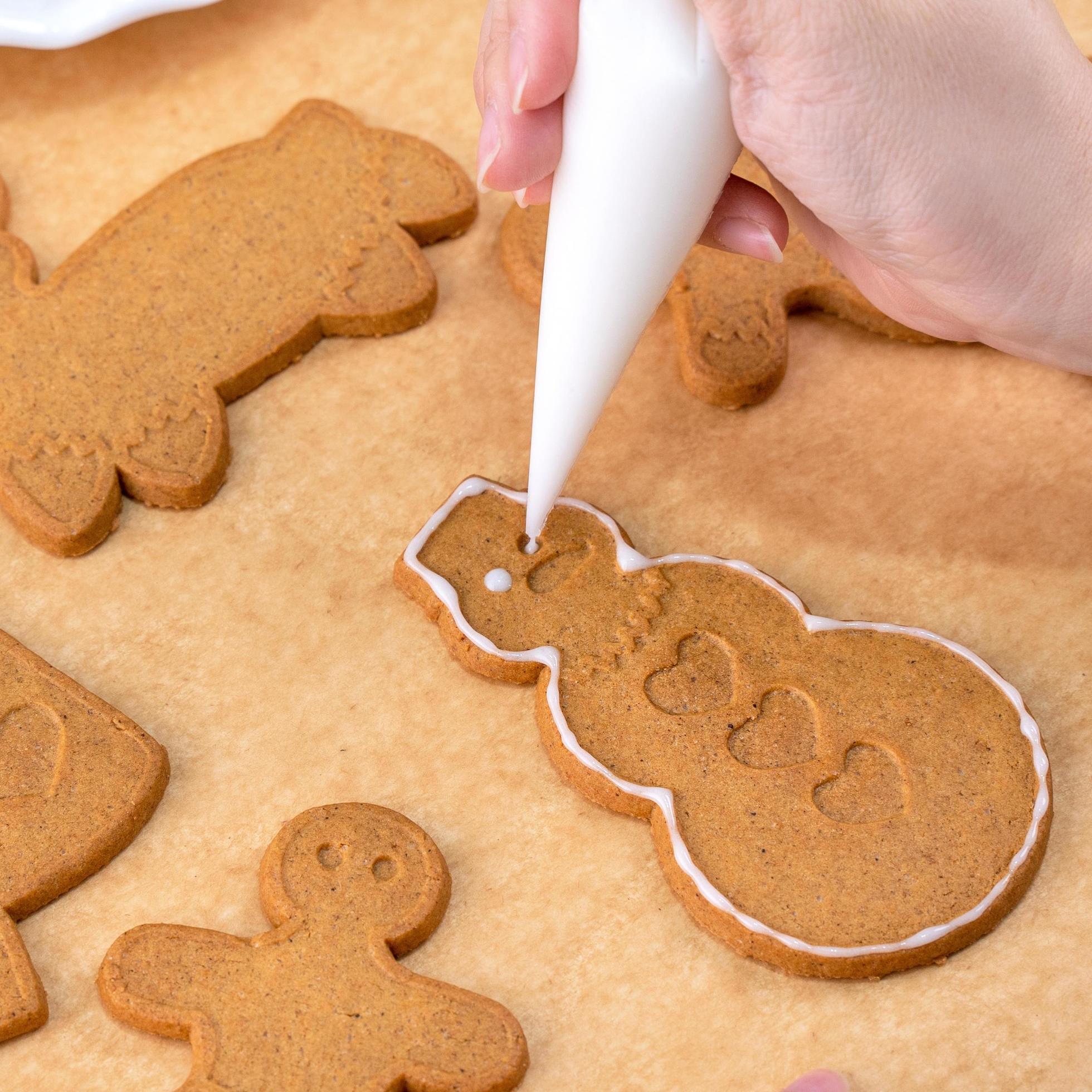 Young woman is decorating Christmas Gingerbread House cookies biscuit at home with frosting topping in icing bag, close up, lifestyle. Stock Free