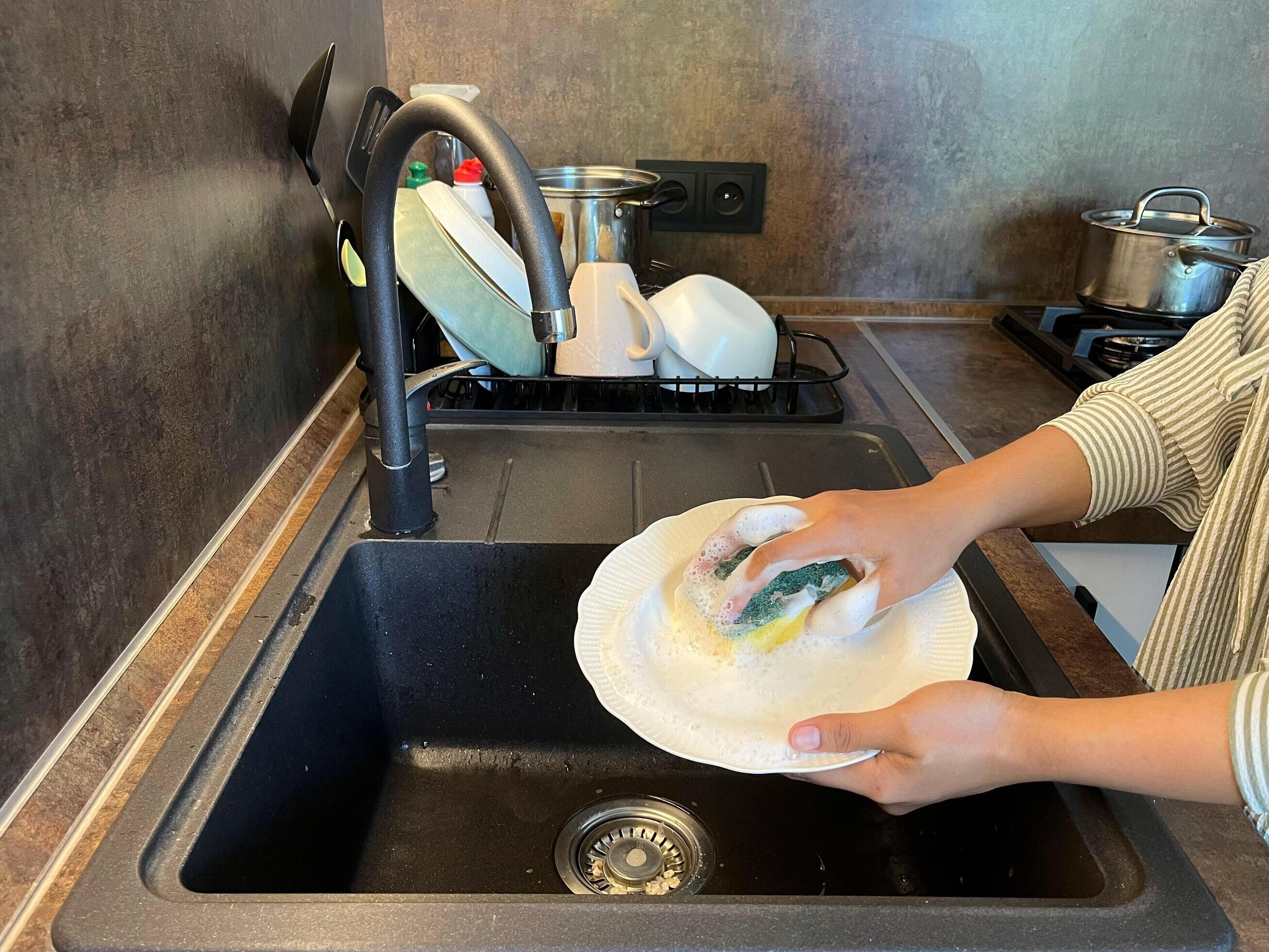 Close up of woman housewife is doing the dishes at home kitchen by using wash sponge and dishwashing soap. Clean the plate Stock Free